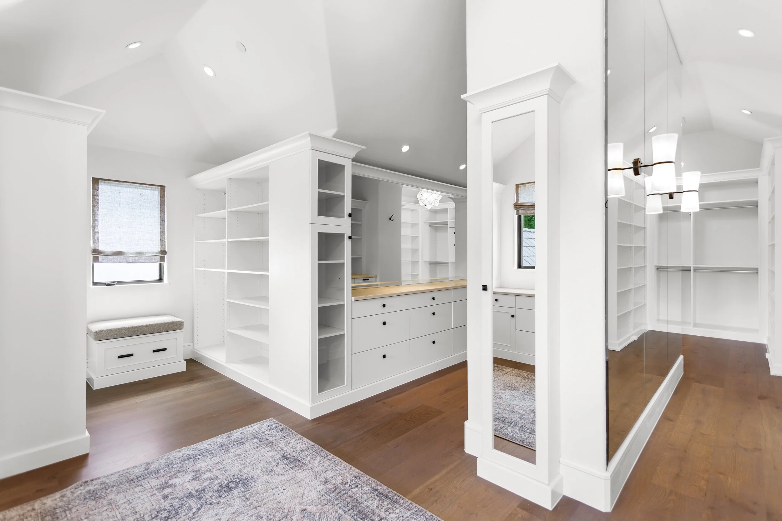 Modern white built-in shelves and cabinetry in a brightly lit room with wooden floors.