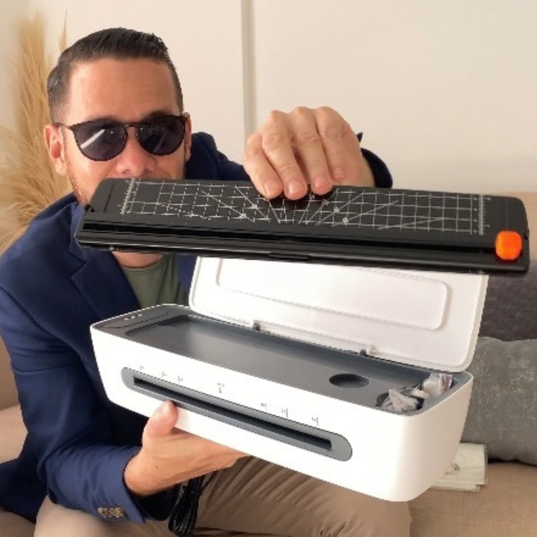 Hombre con gafas negras sosteniendo un cortador de papel y una máquina de escáner o impresora.