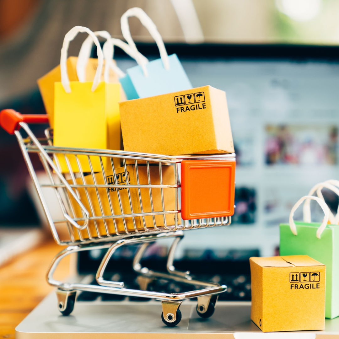 Mini carrito de compras con pequeñas cajas y bolsas de colores, algunas con etiquetas de frágil, en un mostrador.