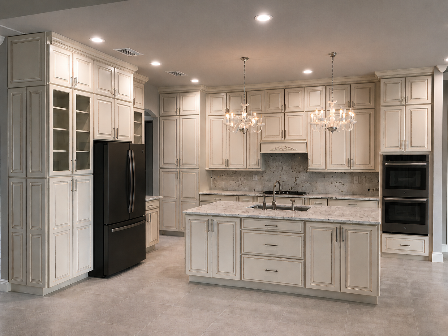 Modern kitchen with white cabinetry, black refrigerator, double ovens, marble island, and chandelier lighting.