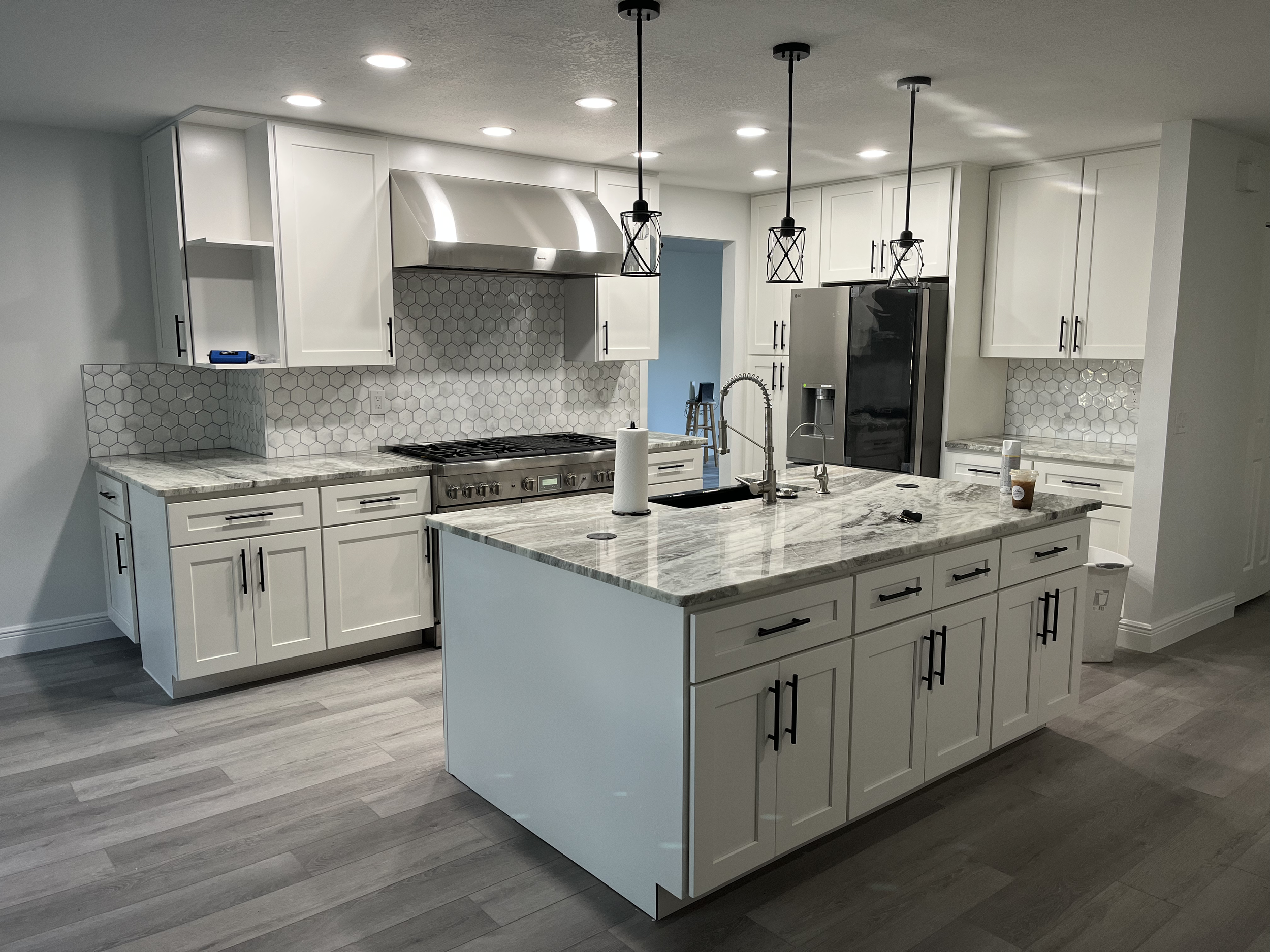 Modern kitchen with white cabinets, a marble island, a stainless steel range hood, a black refrigerator, and pendant lights hanging from the ceiling.
