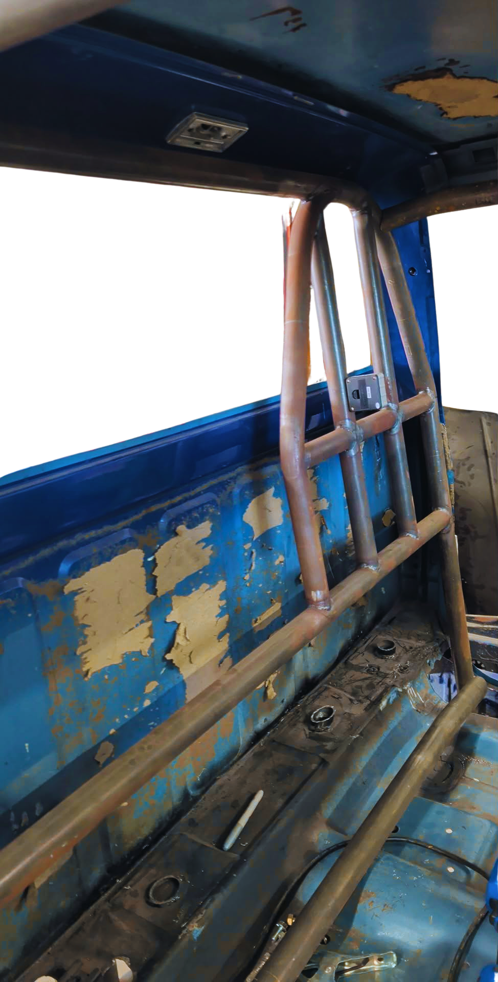 Interior of a vehicle or machinery with rusty roll bars, peeling blue paint, and scattered tools and wires on the floor.