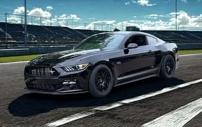Black Ford Mustang driving on a race track with a blue sky and clouds in the background.