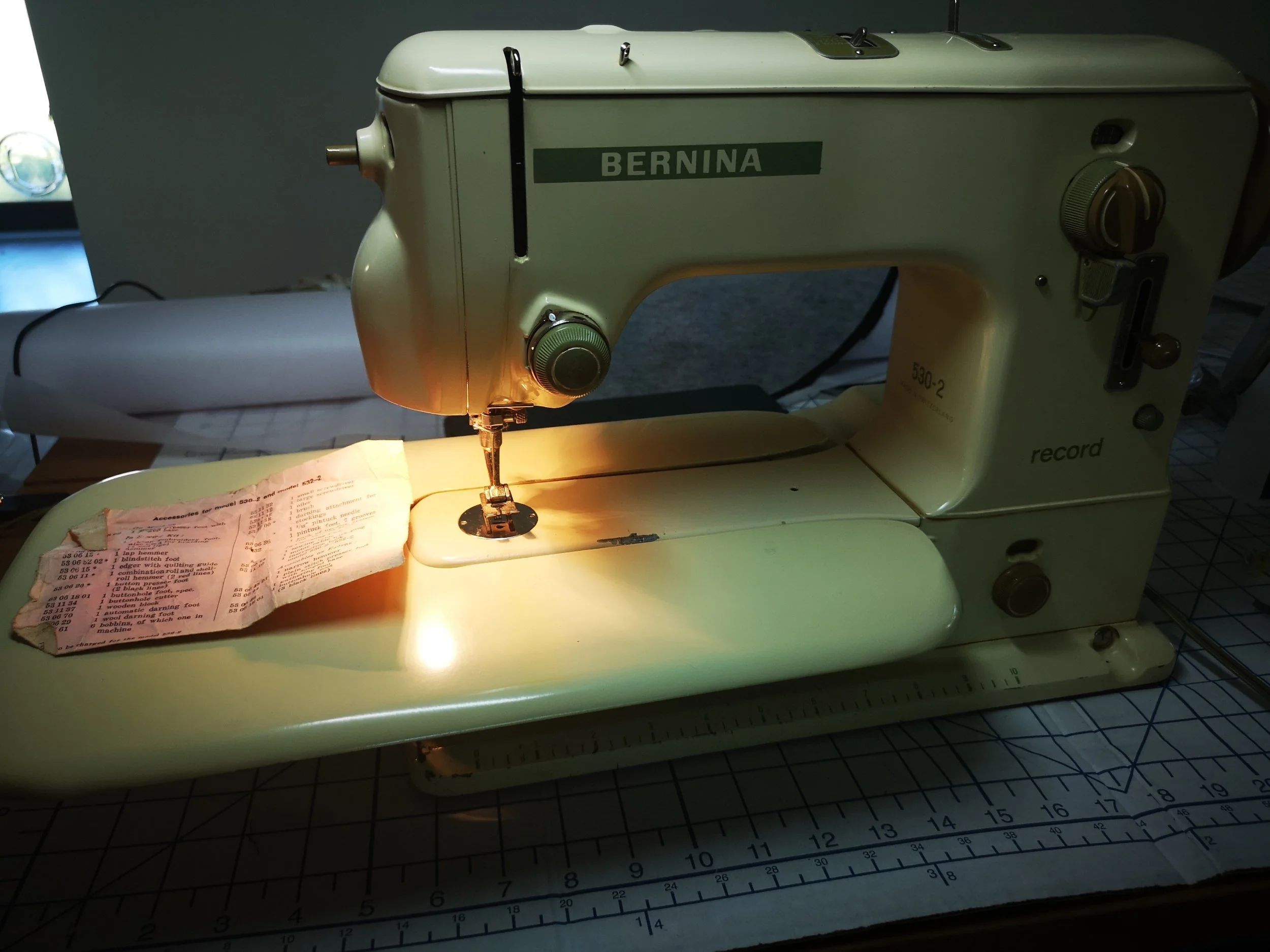 A vintage Bernina sewing machine on a table, with a piece of fabric or paper under the needle, and a ruler marked in inches on the table.