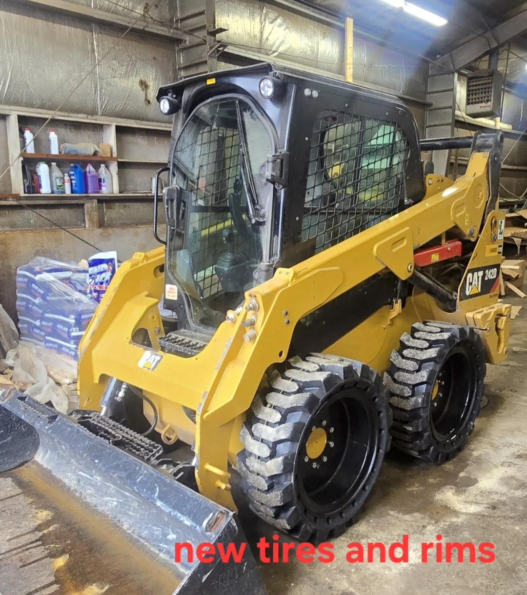 A yellow and black CAT 242D skid-steer loader with new tires and rims inside a workshop or garage.
