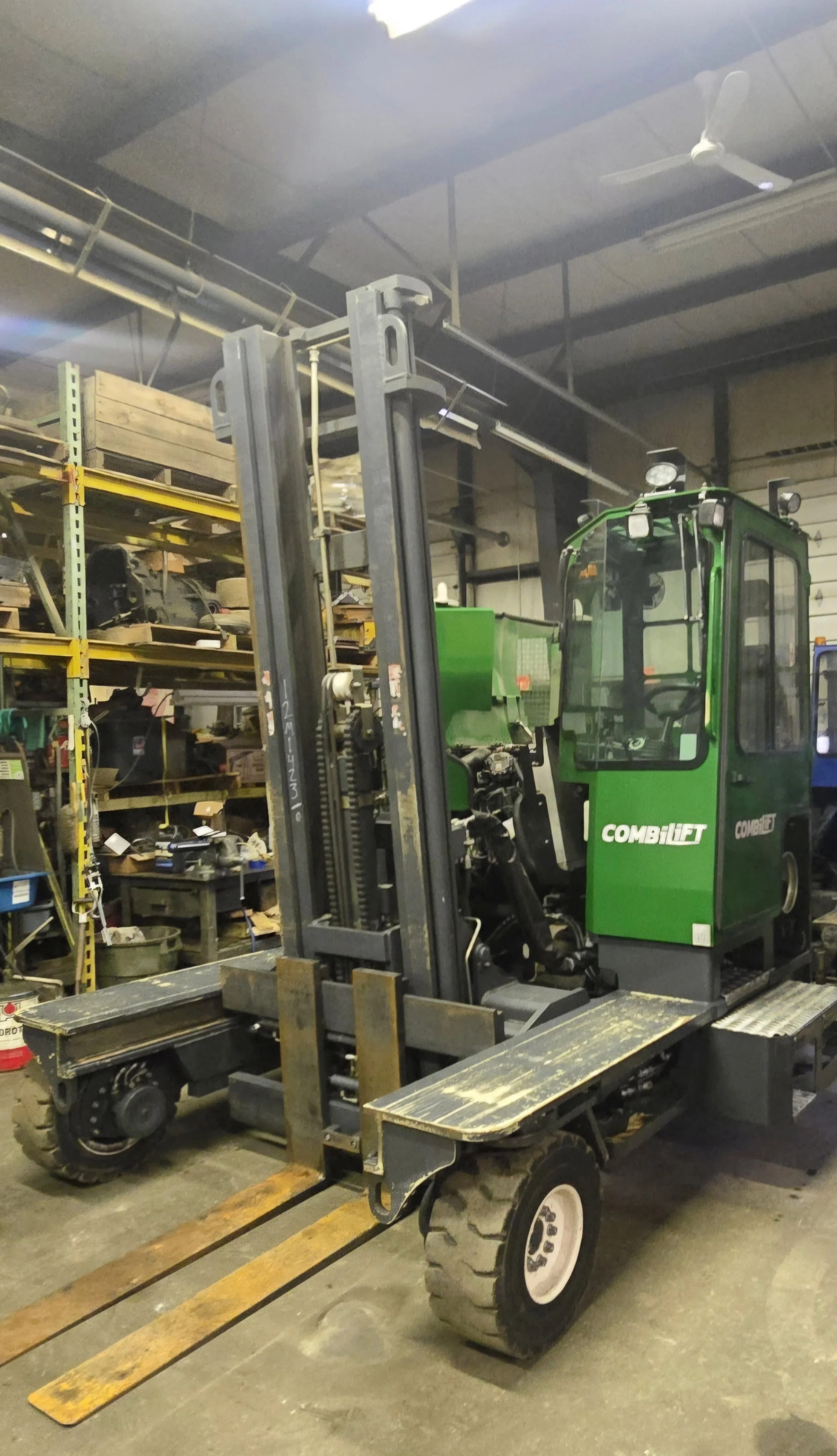 A green and black forklift in a warehouse, surrounded by shelves filled with various items and tools.