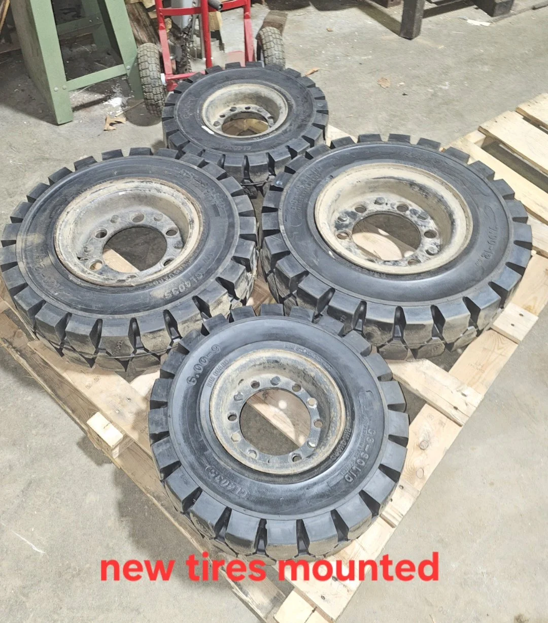 Four large new tires mounted on rims placed on a wooden pallet outdoors.
