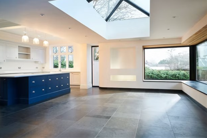 Spacious, modern living area with large windows, a skylight, and an open white and blue kitchen.