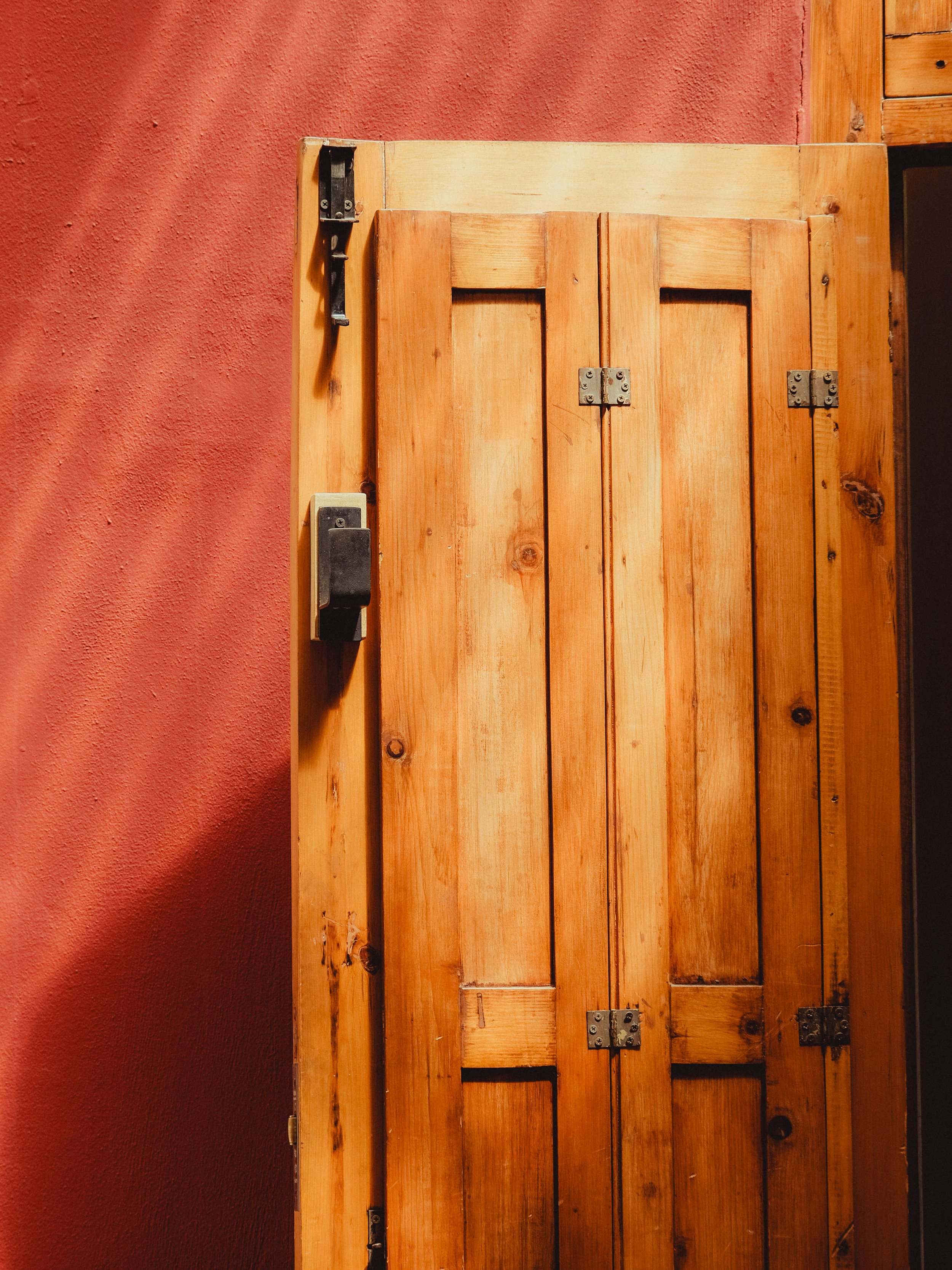 Wooden door with black hinges and a lock, against a textured red wall.