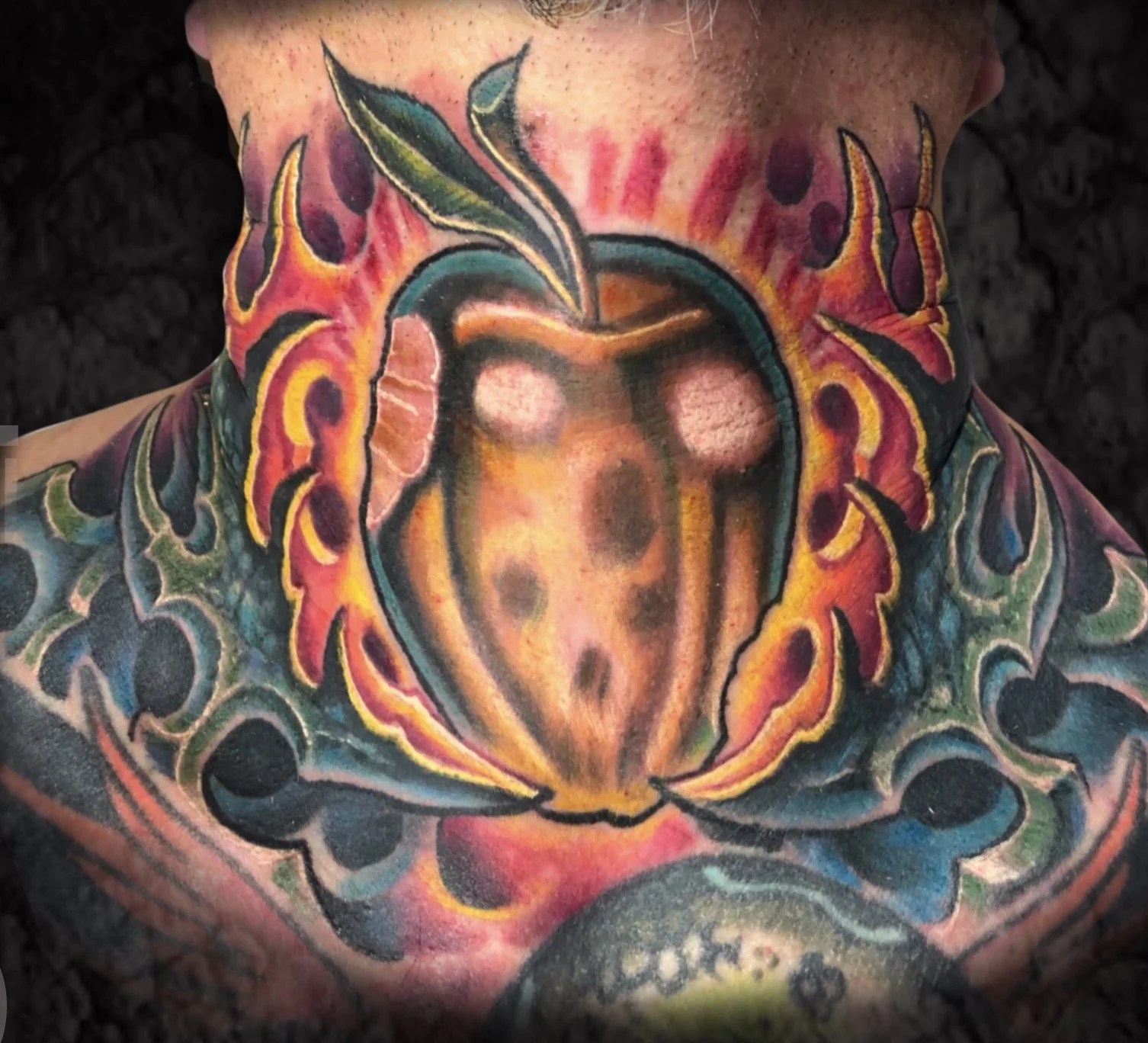 Colorful tattoo of a heart with flames and a leaf on the neck, surrounded by decorative patterns.