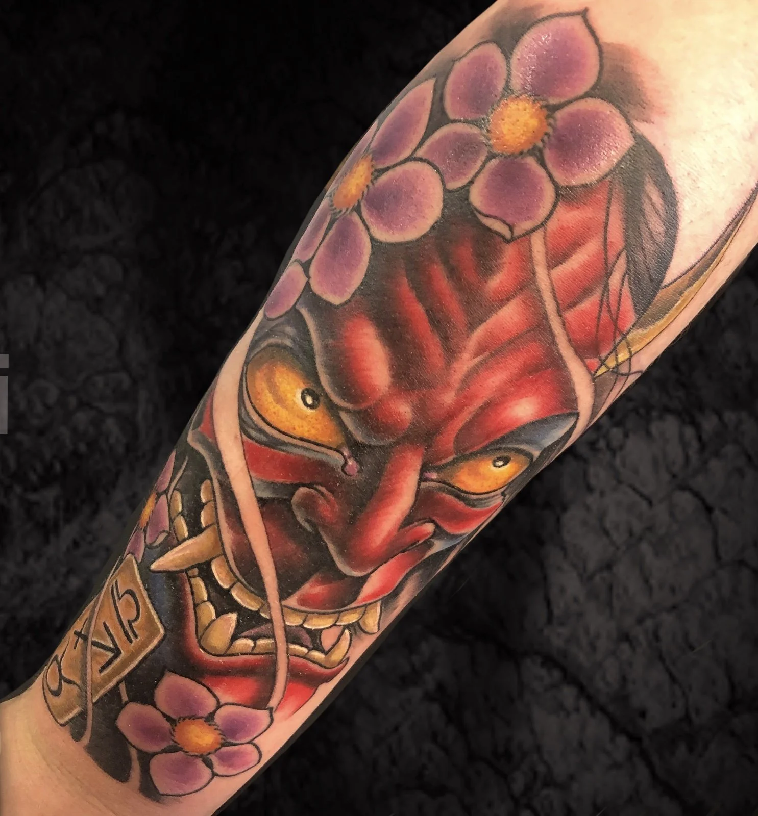 Tattoo of a red dragon with purple flowers and yellow eyes on an arm.