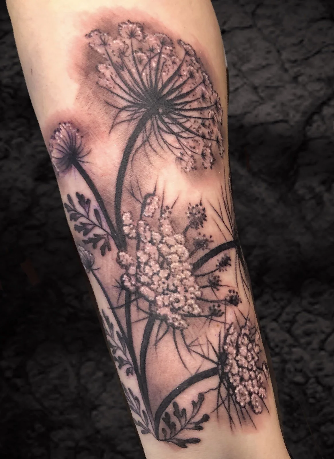 Black and gray tattoo of various flowering plants on a person's arm.