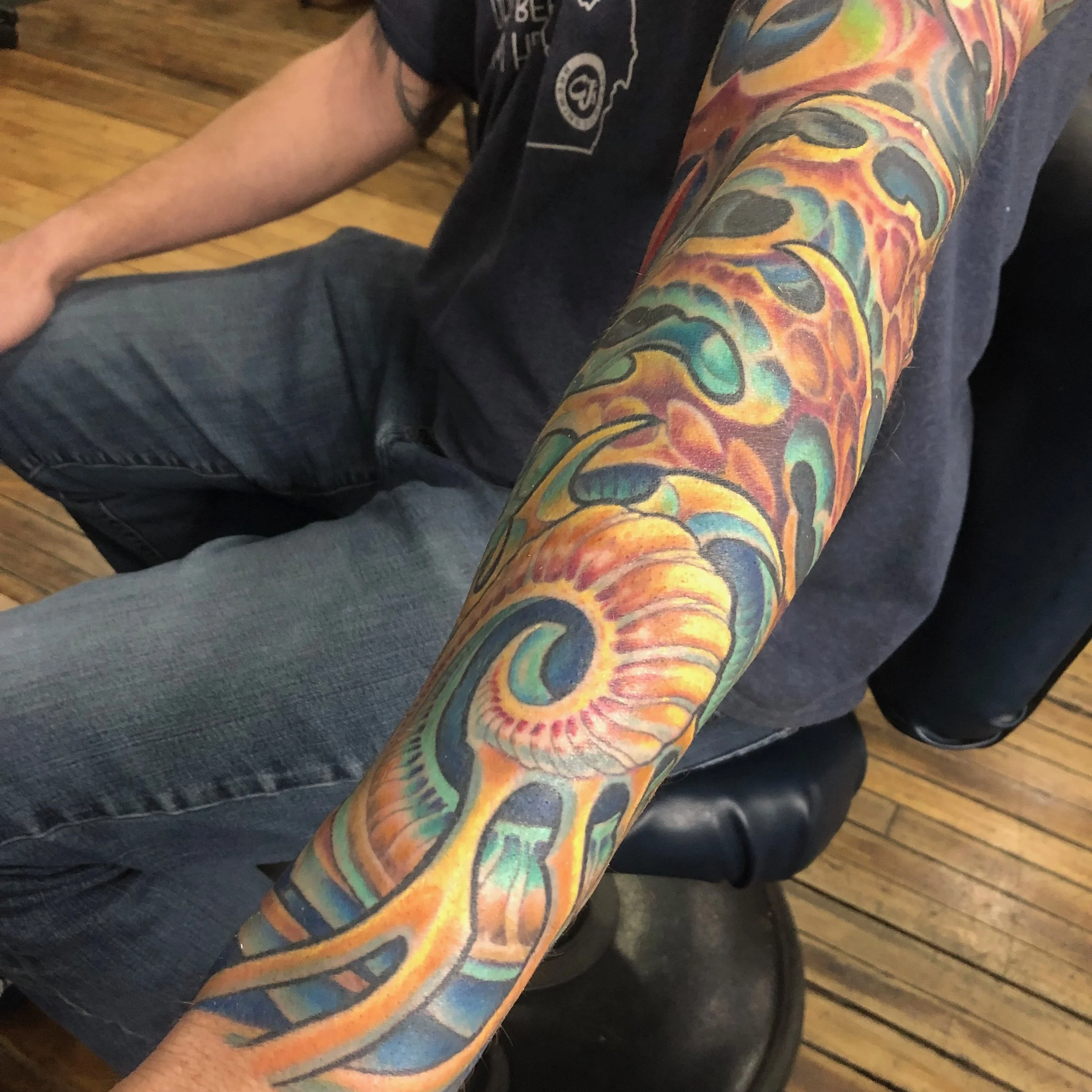 Colorful dragon tattoo sleeve on a person's arm, featuring vivid shades of orange, yellow, green, and black, with intricate scales and patterns.