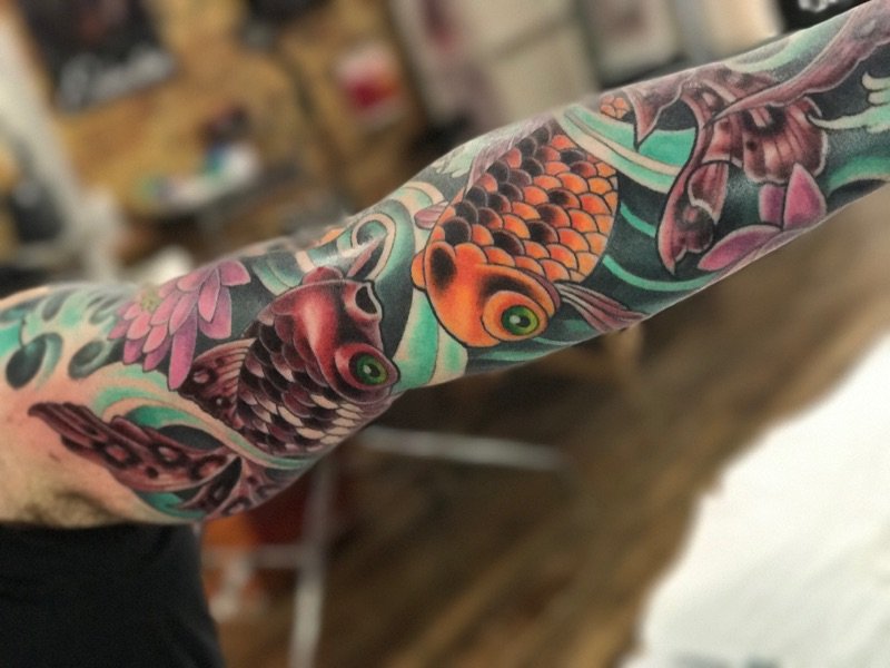 Colorful tattoo of koi fish on person's arm, featuring vibrant orange, pink, and green hues.