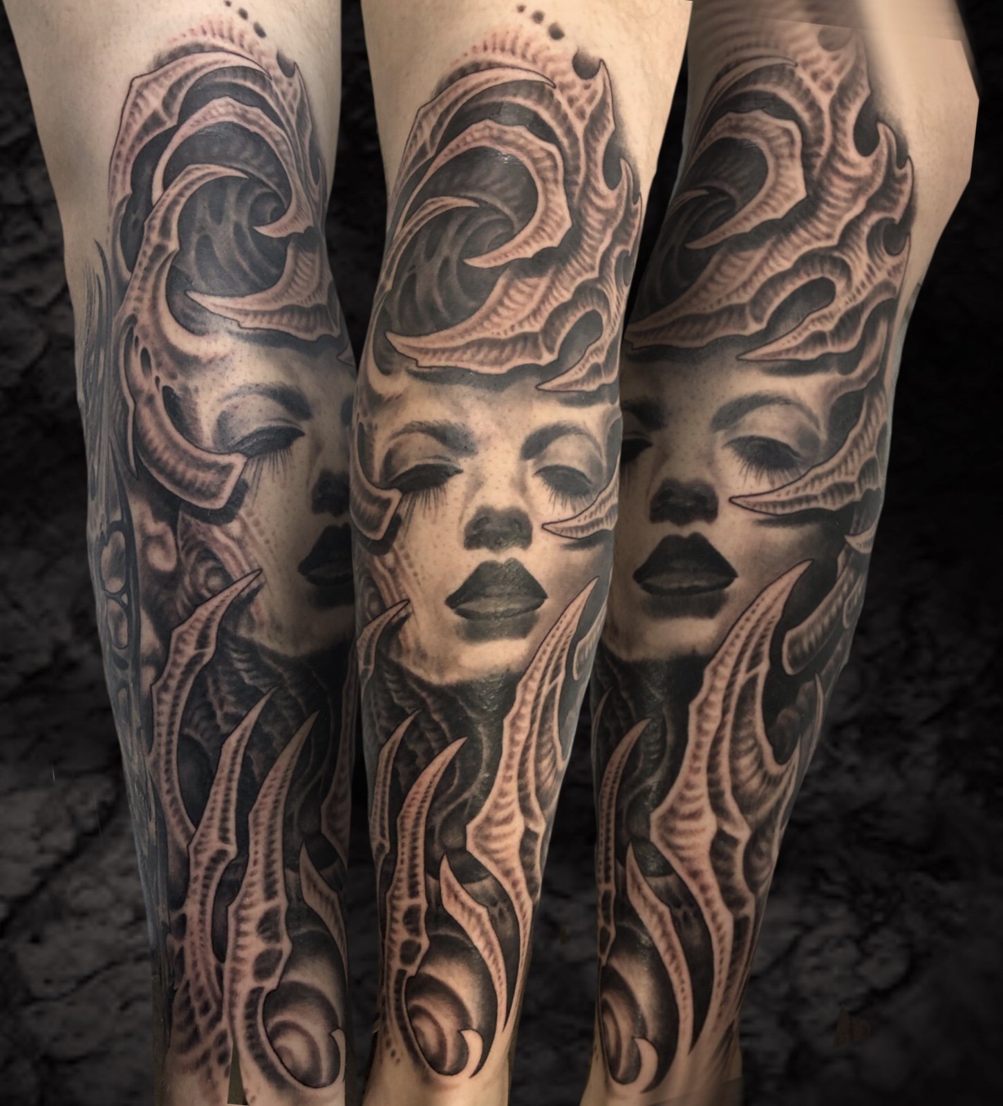 Tattoo artwork on person's legs featuring a woman's face with closed eyes, surrounded by stylized waves and abstract patterns in black and gray ink.