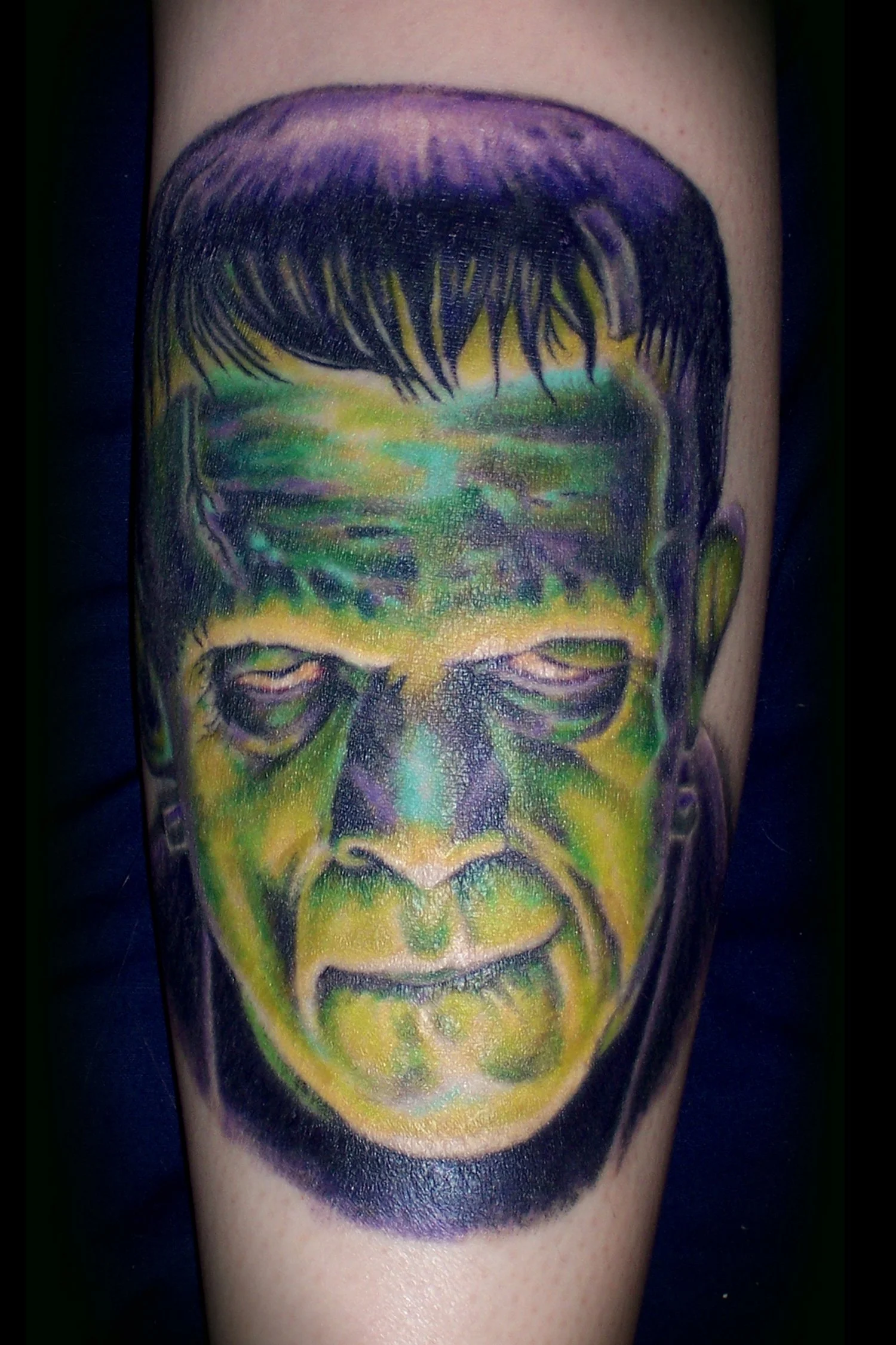 Tattoo of a stylized face with green, yellow, purple, and black colors.