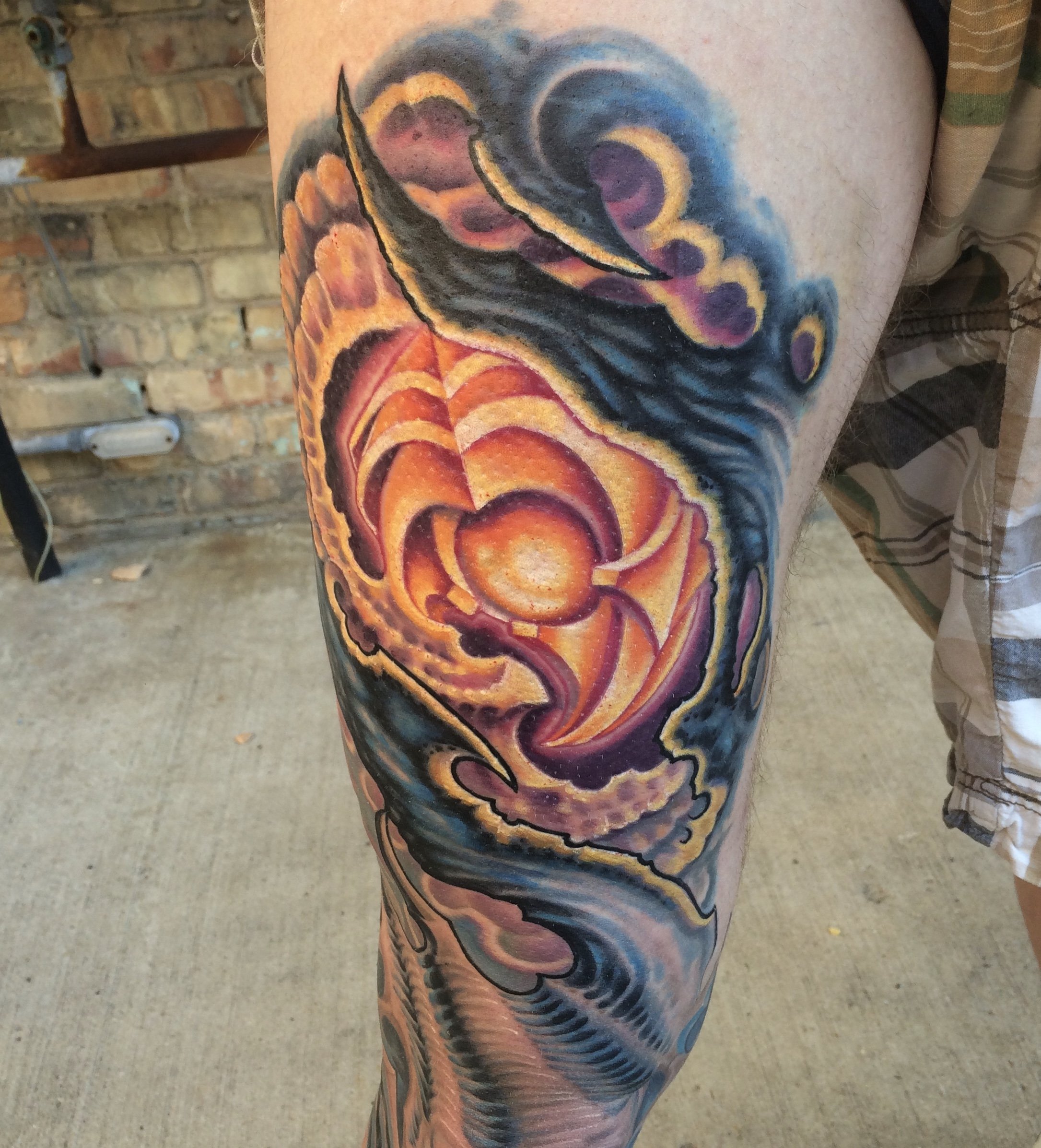 Colorful tattoo of a rainbow-colored dragon on a person's leg, with fiery hues of orange, pink, purple, and blue, set against a background of dark blue and black swirling clouds.