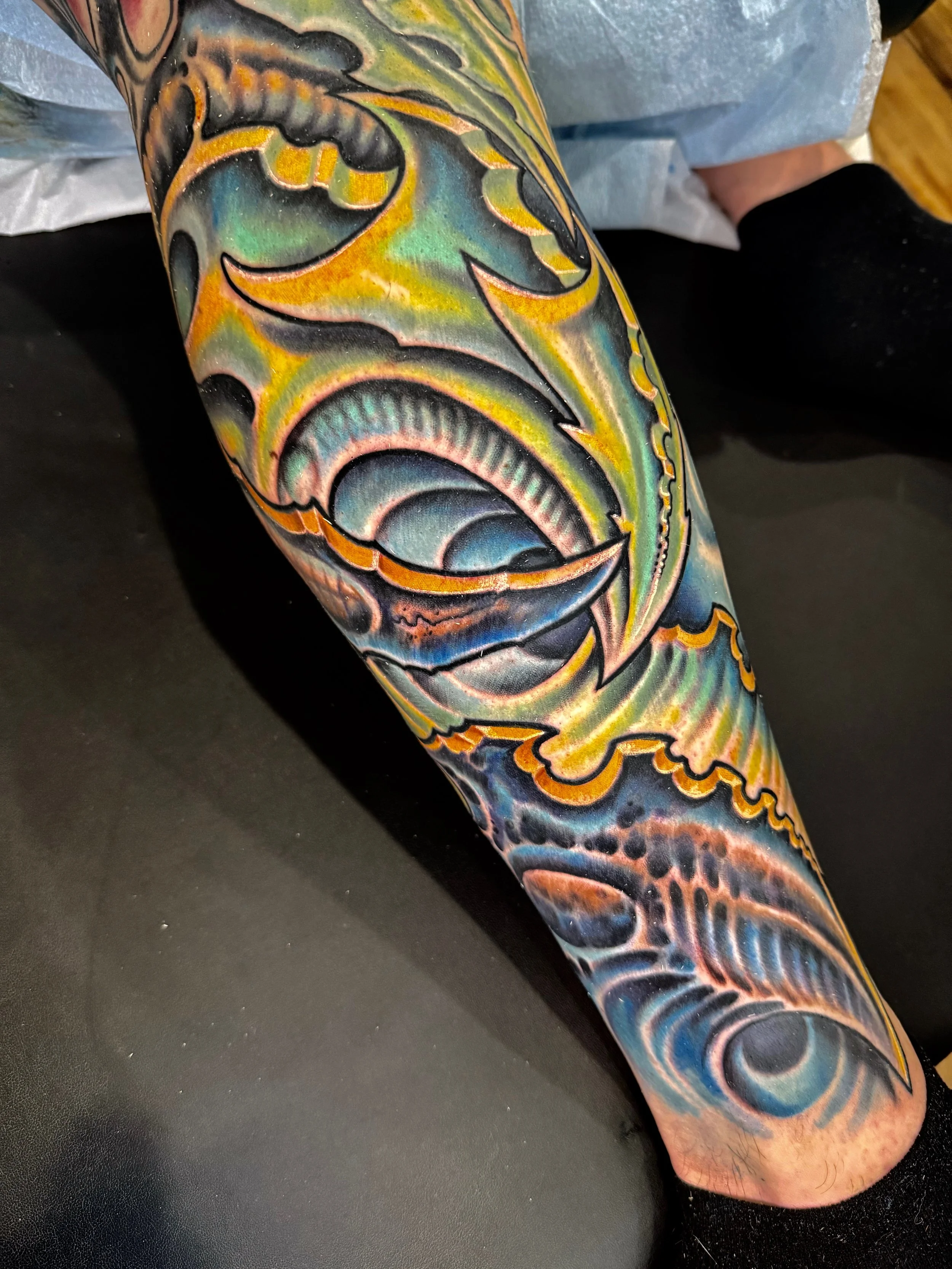 A portrait tattoo on the arm depicting a dolphin with colorful, abstract background patterns in shades of blue, green, yellow, and orange.