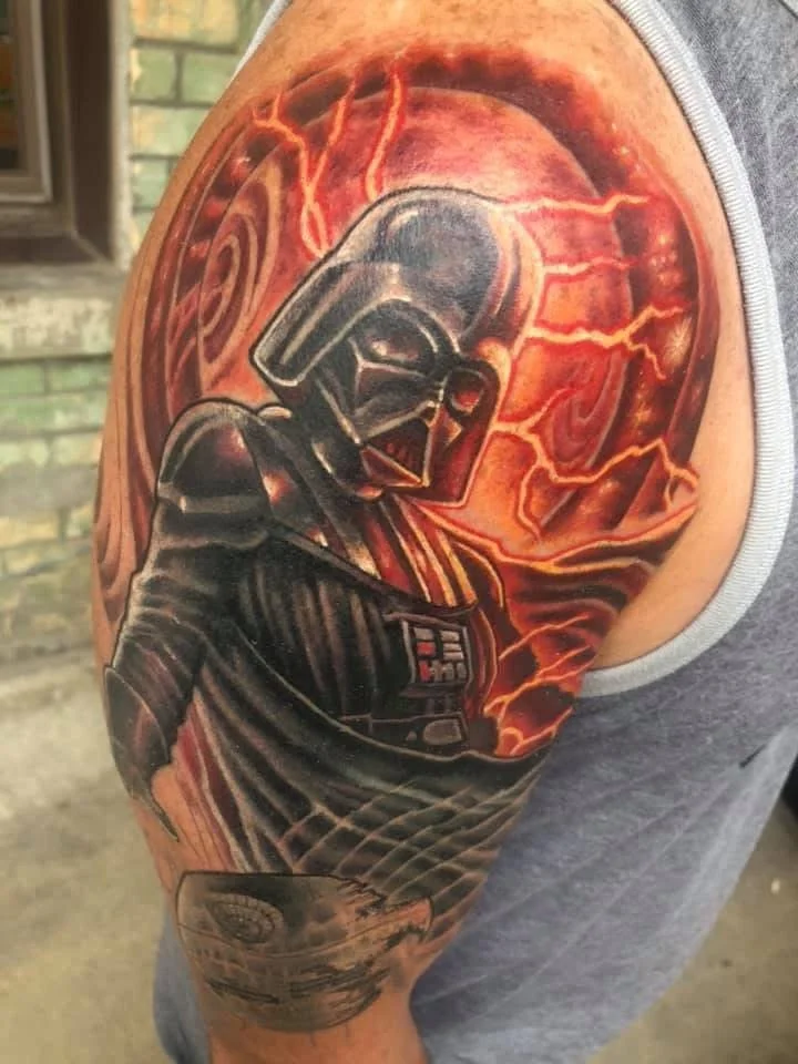 Tattoo of Darth Vader from Star Wars with lightning and a planet in the background on upper arm.