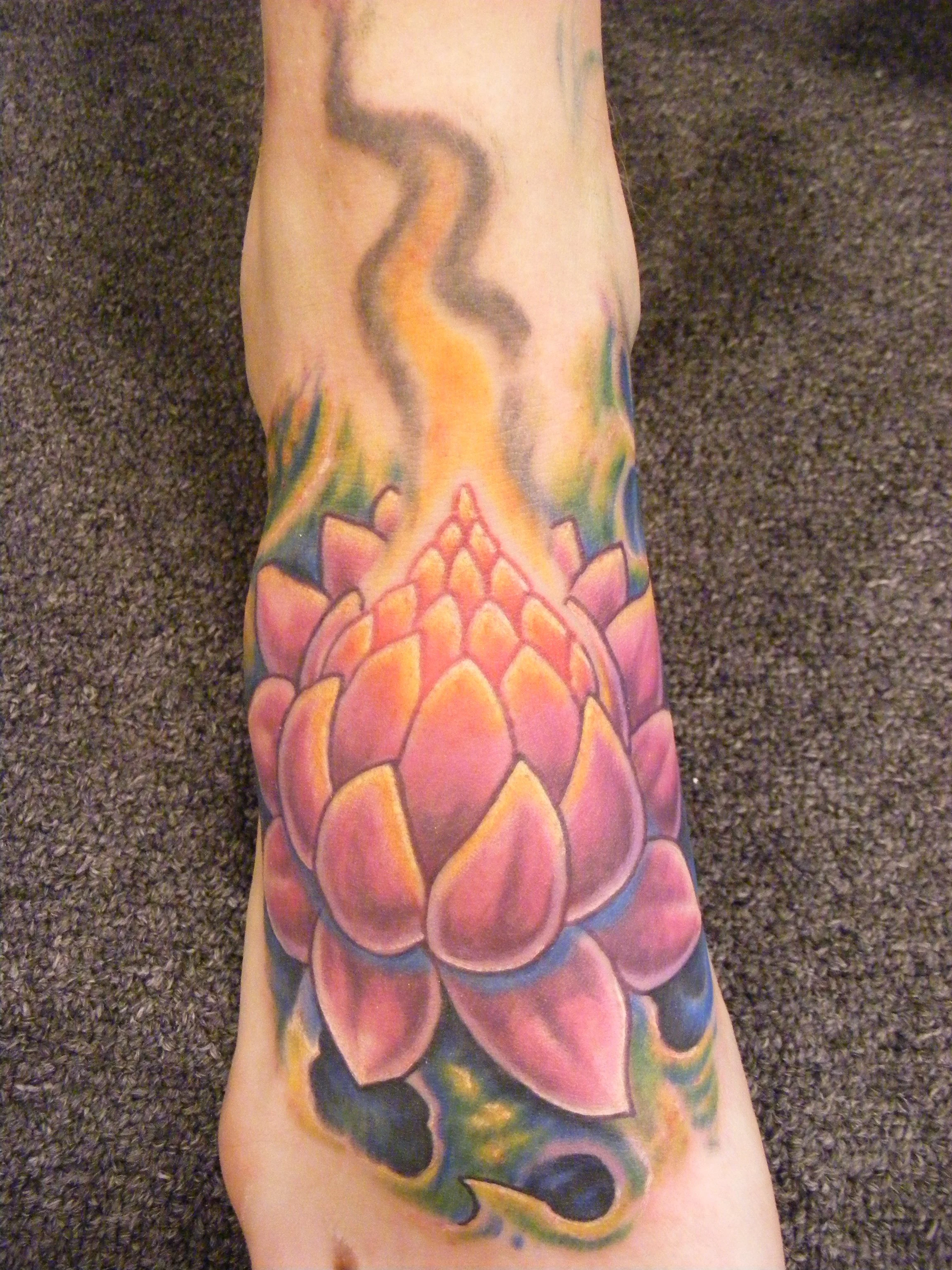 Colorful tattoo of a lotus flower on a person's arm, with vibrant pink, orange, and green hues.