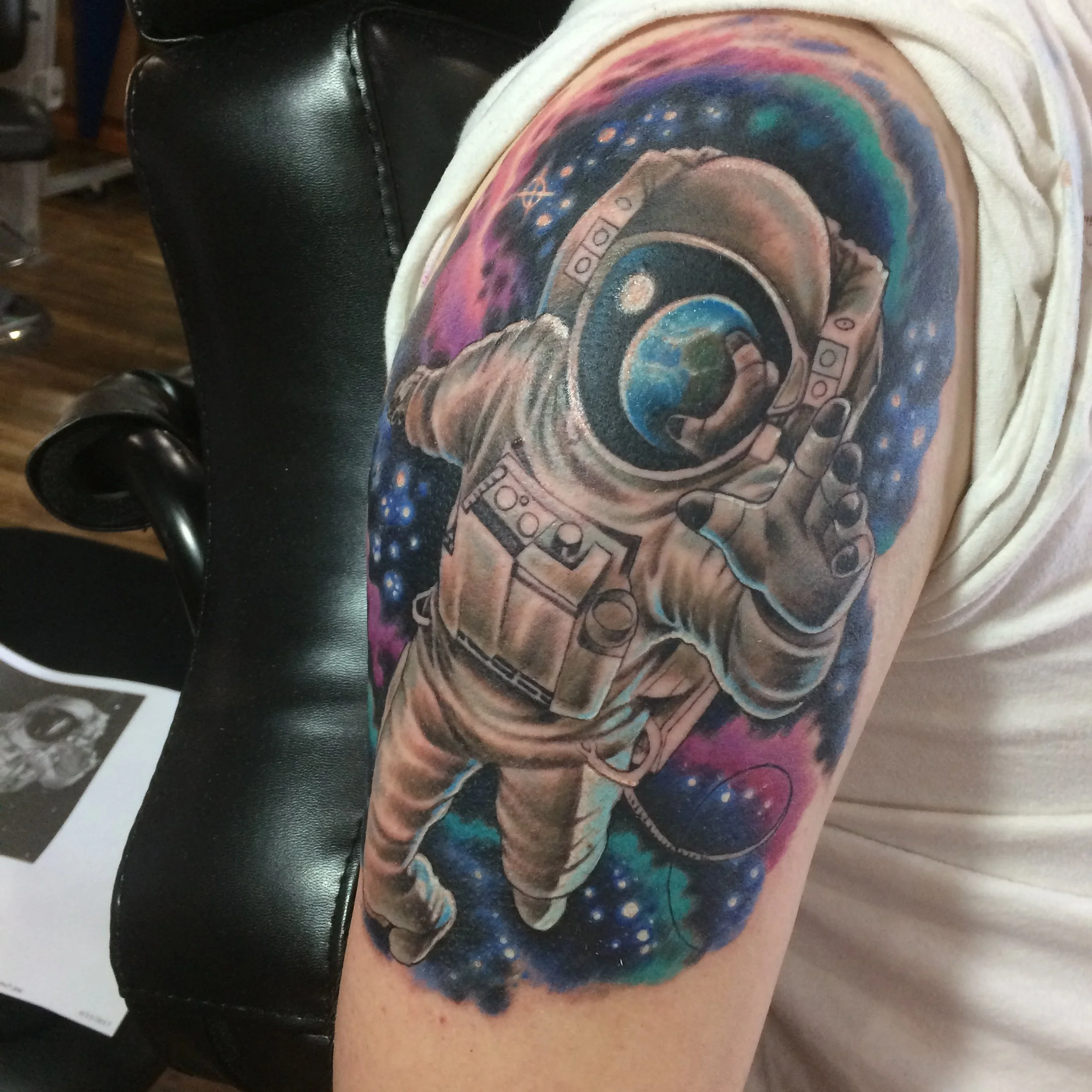 Colorful galaxy-themed tattoo on person's shoulder featuring a spaceship, planets, and cosmic elements.