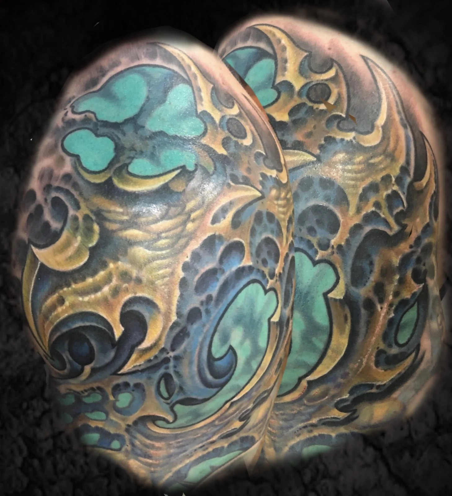 Close-up of a person's skin covered in colorful tattoo art, featuring black outlines, green heart-shaped designs, and gold accents.