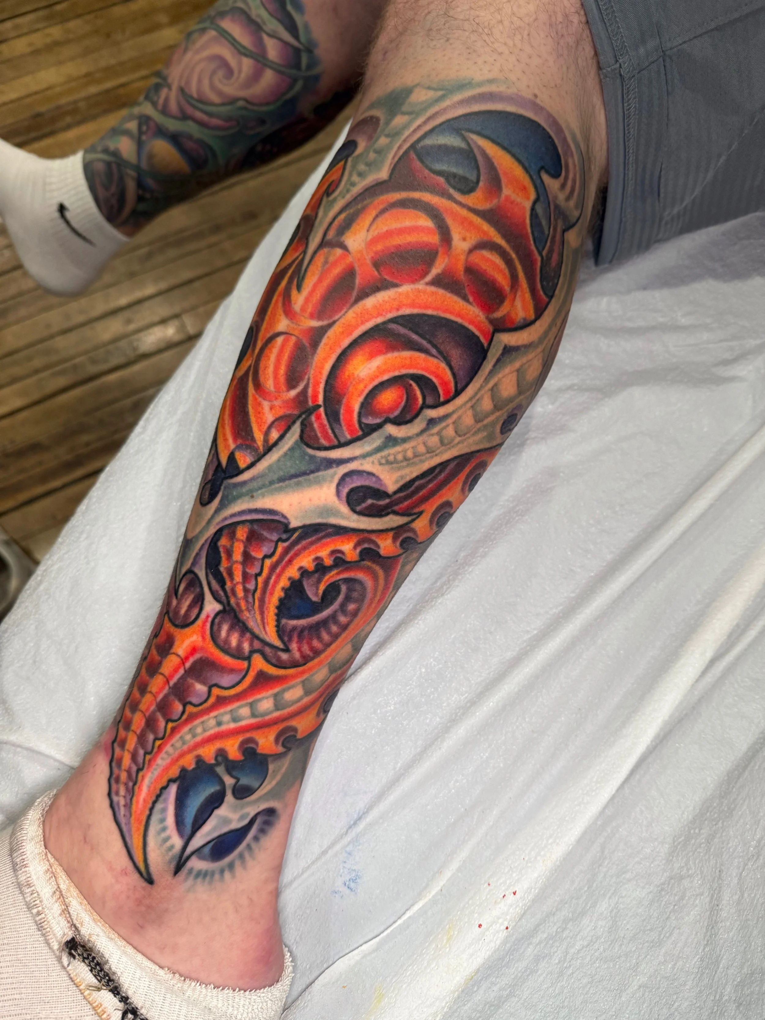 Colorful tattoo sleeve on person's arm featuring abstract and swirling designs with shades of orange, purple, and black, extending from the shoulder to the forearm.