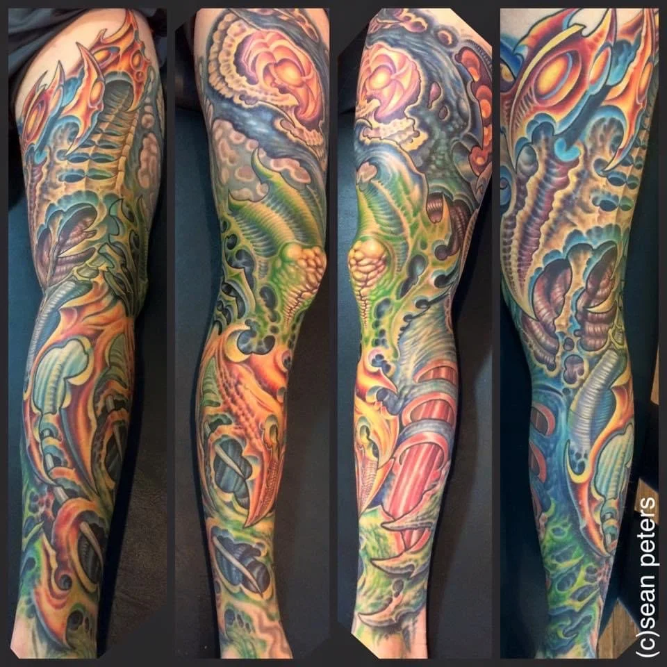 Colorful full sleeve tattoo featuring a dragon, flames, clouds, and abstract designs in shades of orange, green, blue, and purple.