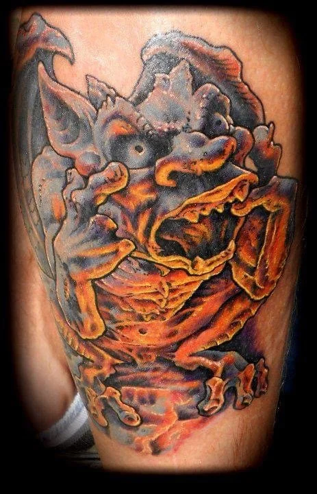 Colorful tattoo of a goblin or demon with exaggerated features and pointed ears on a person's arm.