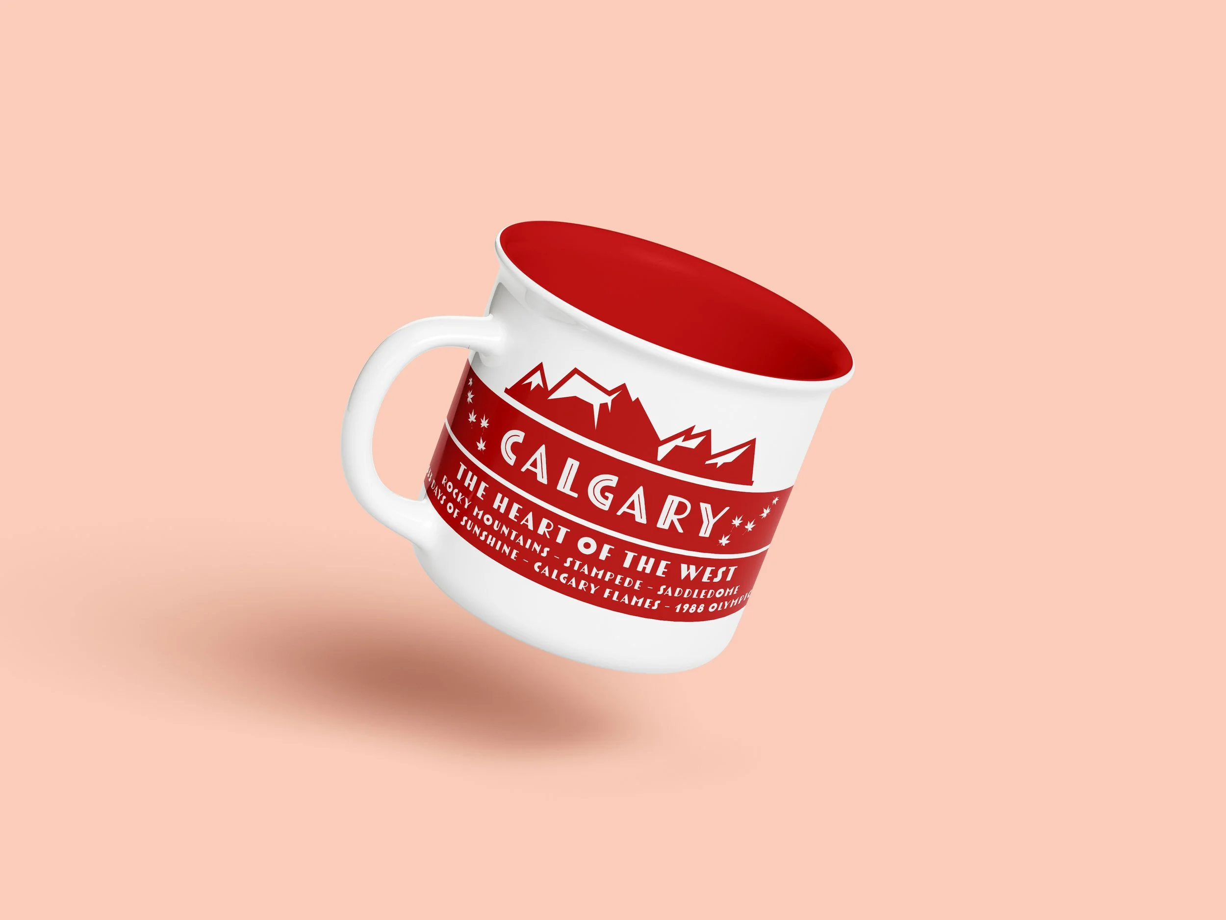 A white ceramic mug with red interior and red exterior featuring white mountain and maple leaf designs and a list of Canadian cities, including Calgary, Stampeded, Sadledeomie, and Vancouver, on a peach background.