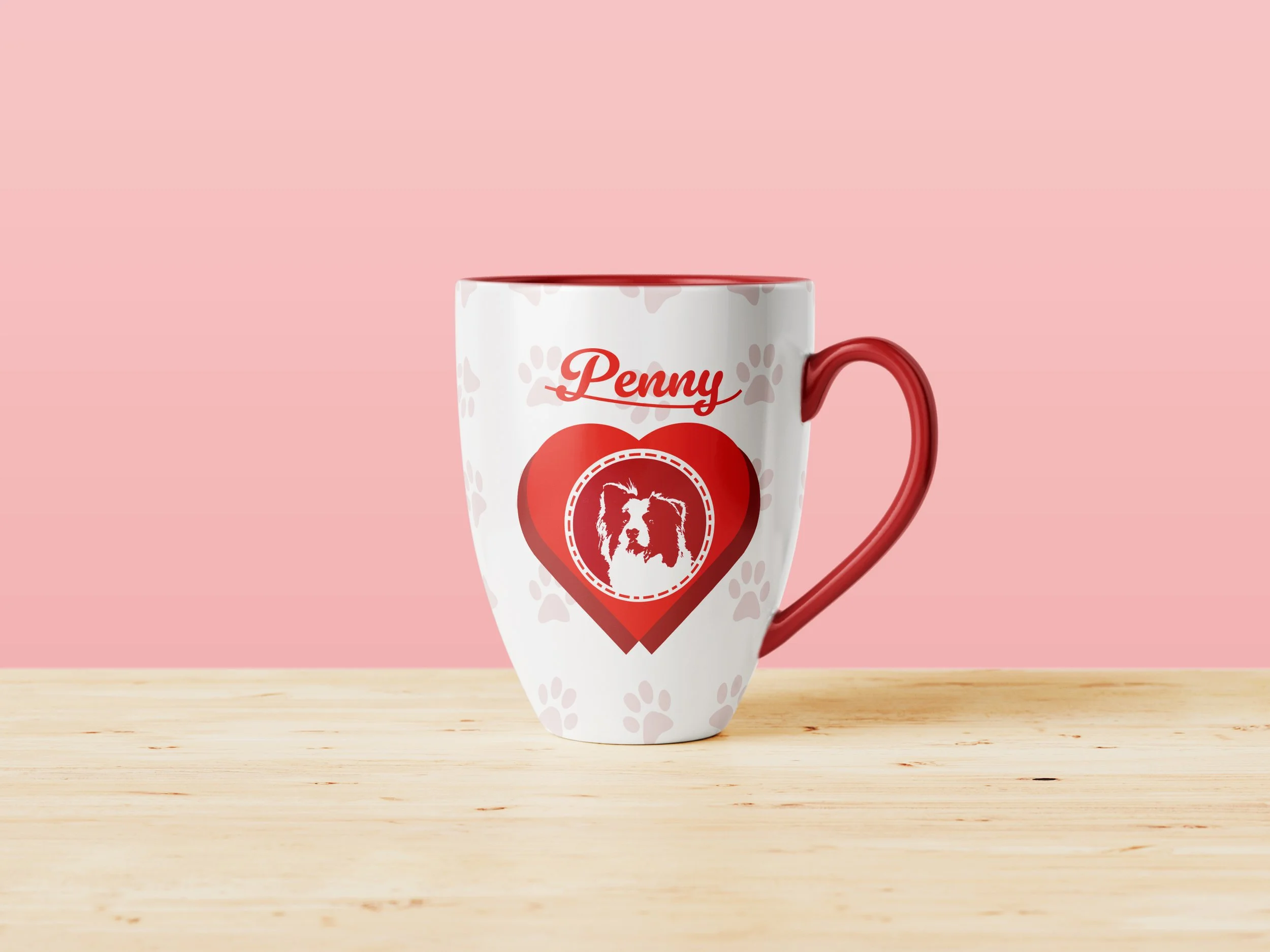 White ceramic mug with a red handle and red interior, featuring a heart-shaped design with a dog image and the word "Penny" written above, placed on a wooden surface against a light pink background.