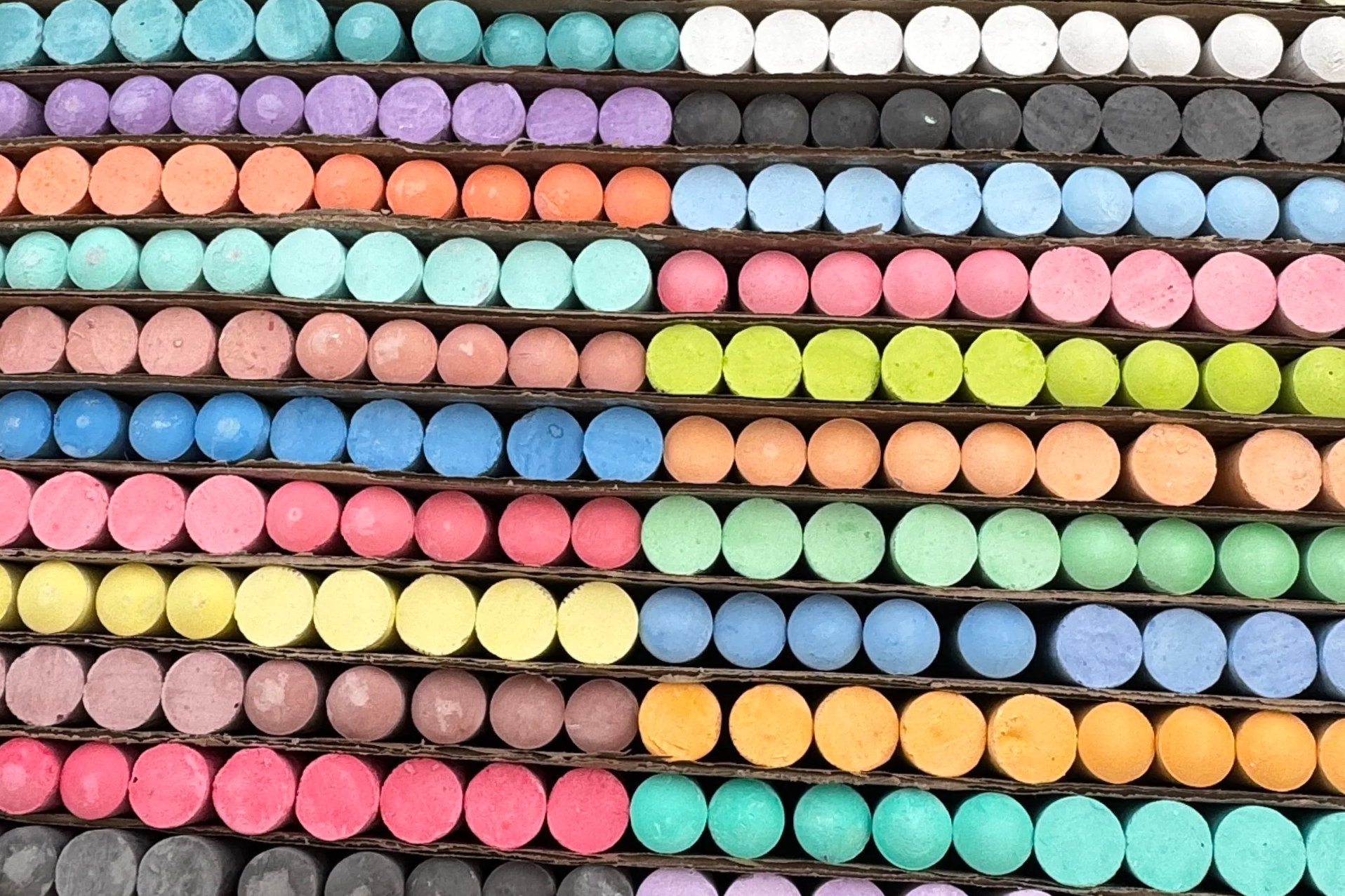 Colorful chalk sticks organized in rows in a cardboard holder.