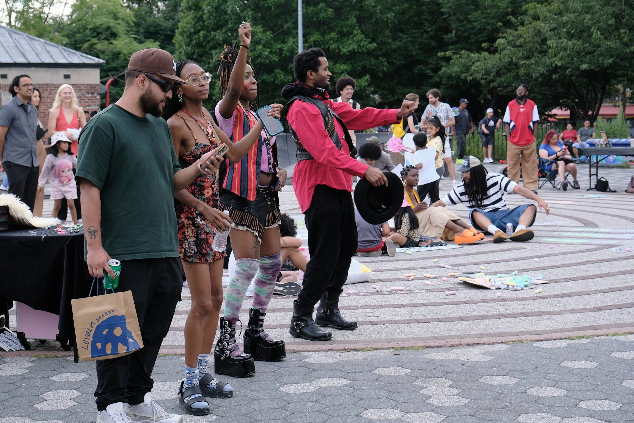 A diverse group of people participating in an outdoor event, with some wearing platform shoes, standing in line or spacing apart, with trees and other attendees in the background.