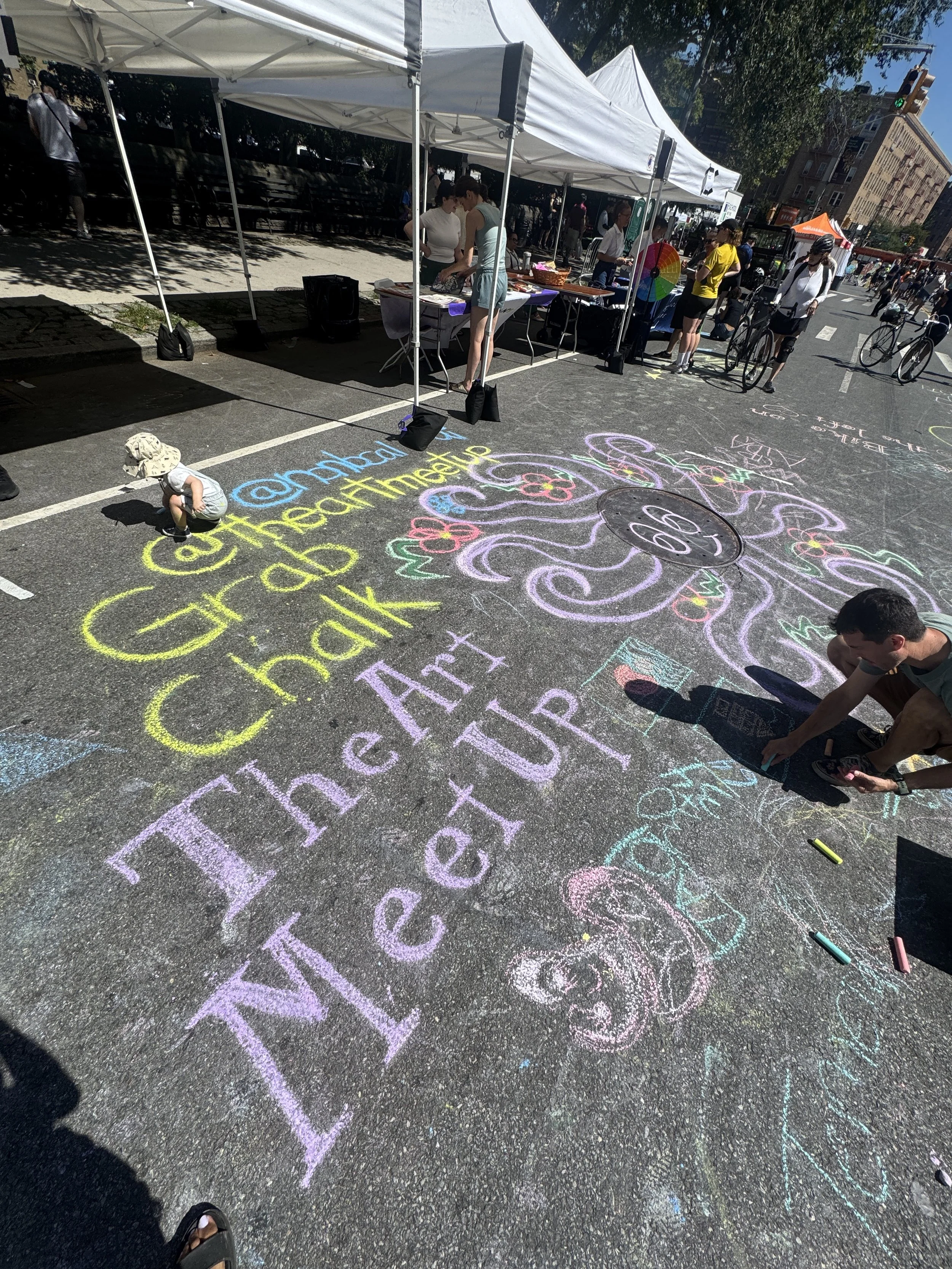 Colorful chalk drawings and writings on the street, with people participating in an outdoor event under tents.