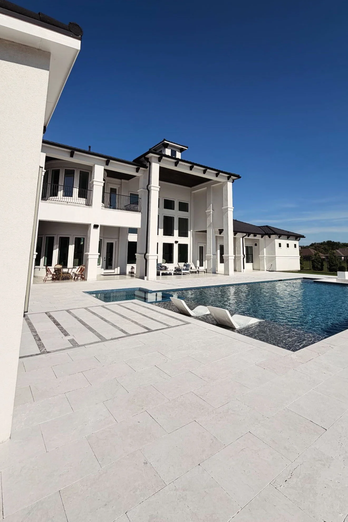 Modern white house with a backyard pool, outdoor furniture, and a spacious patio under a clear blue sky.