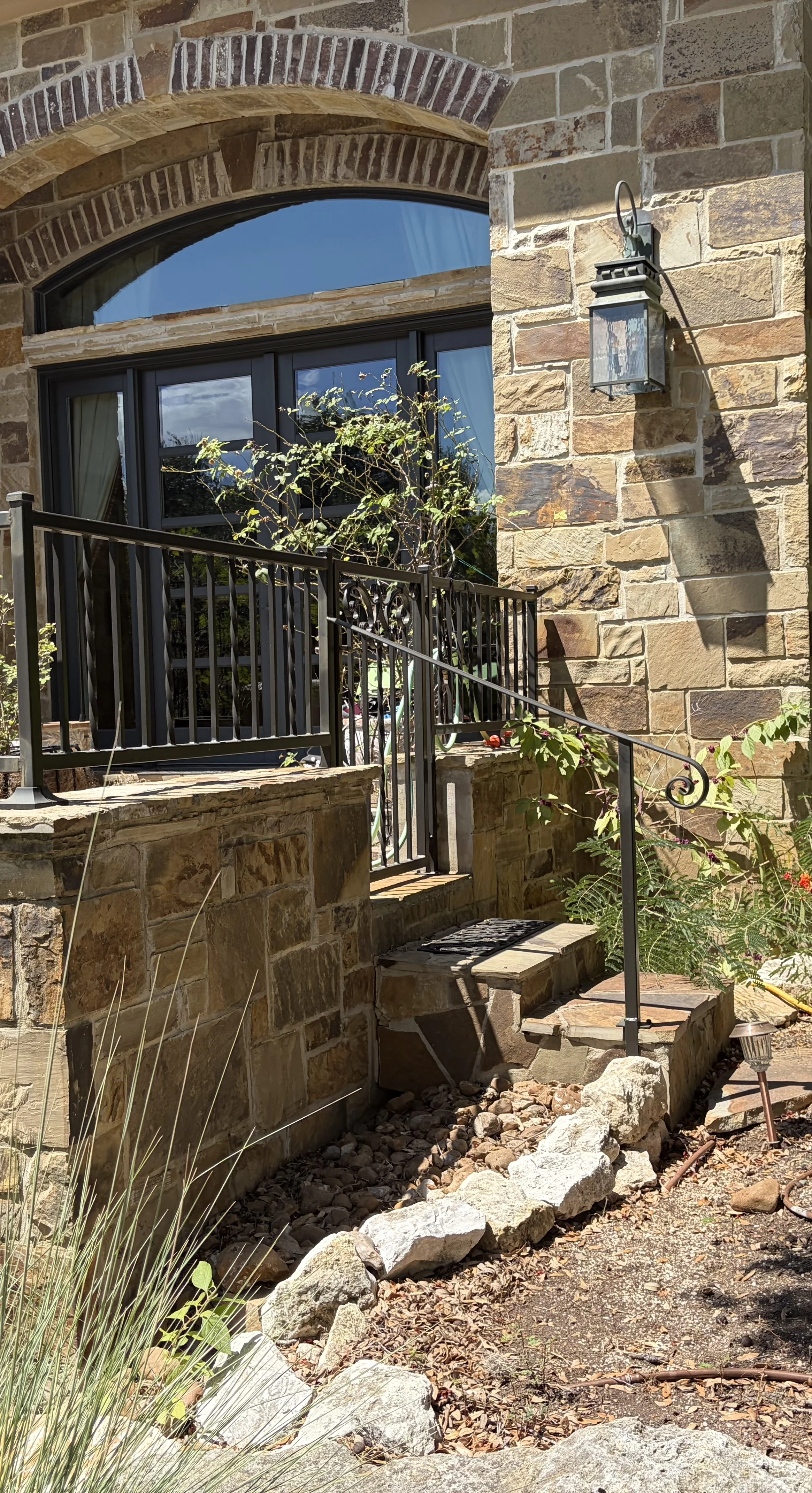  A ornamental wrought iron gate and hand rail in a small entry way leading to courtyard in front of stone house.