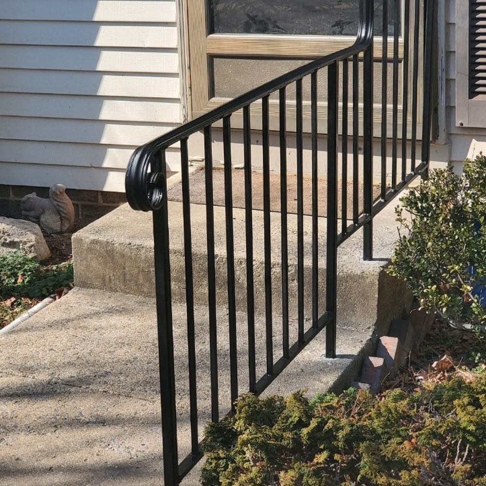 A black metal railing installed along outdoor concrete steps leading to a house door.