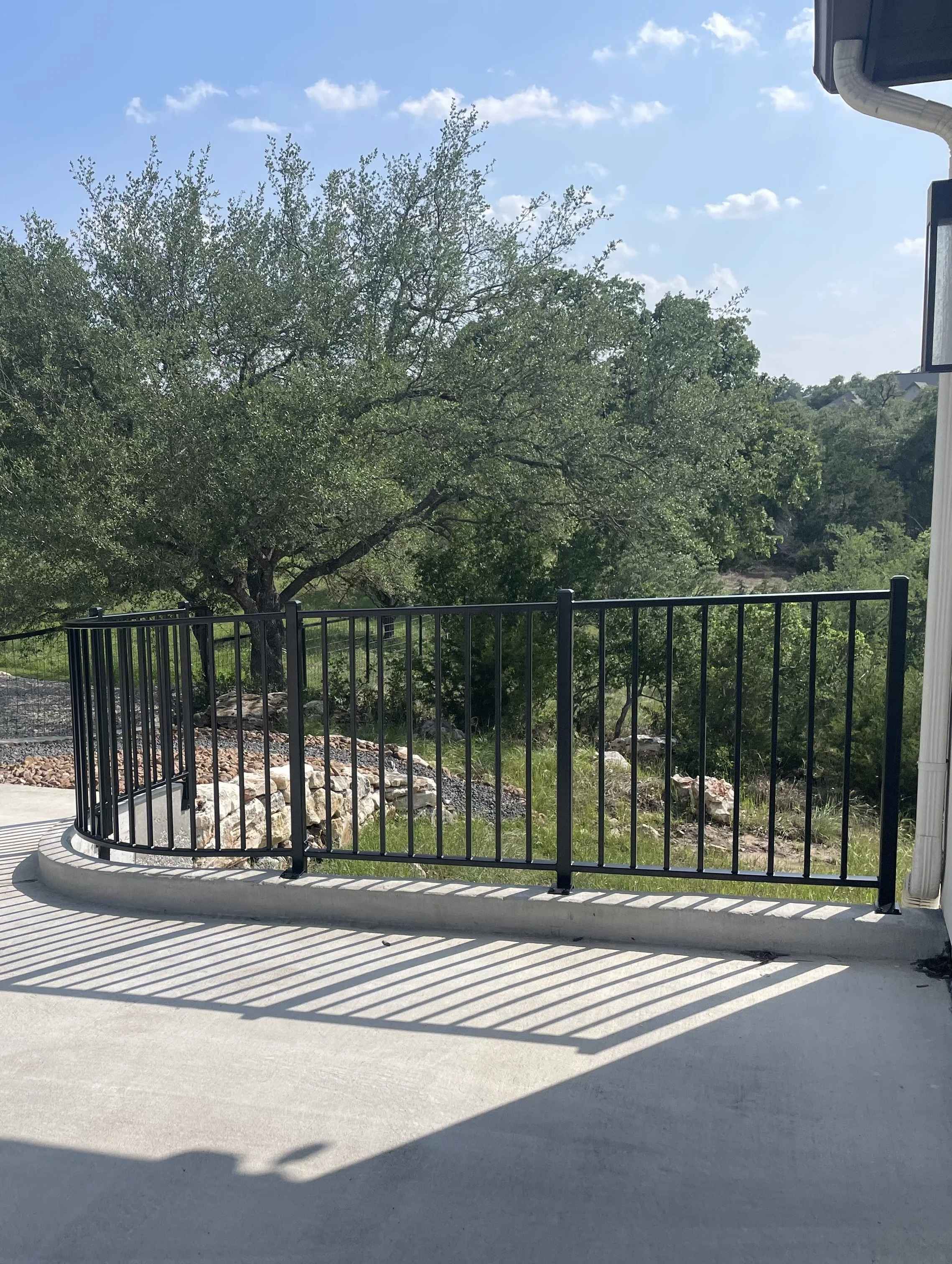 Black metal wrought iron railing on curved edge of driveway to garage of house.
