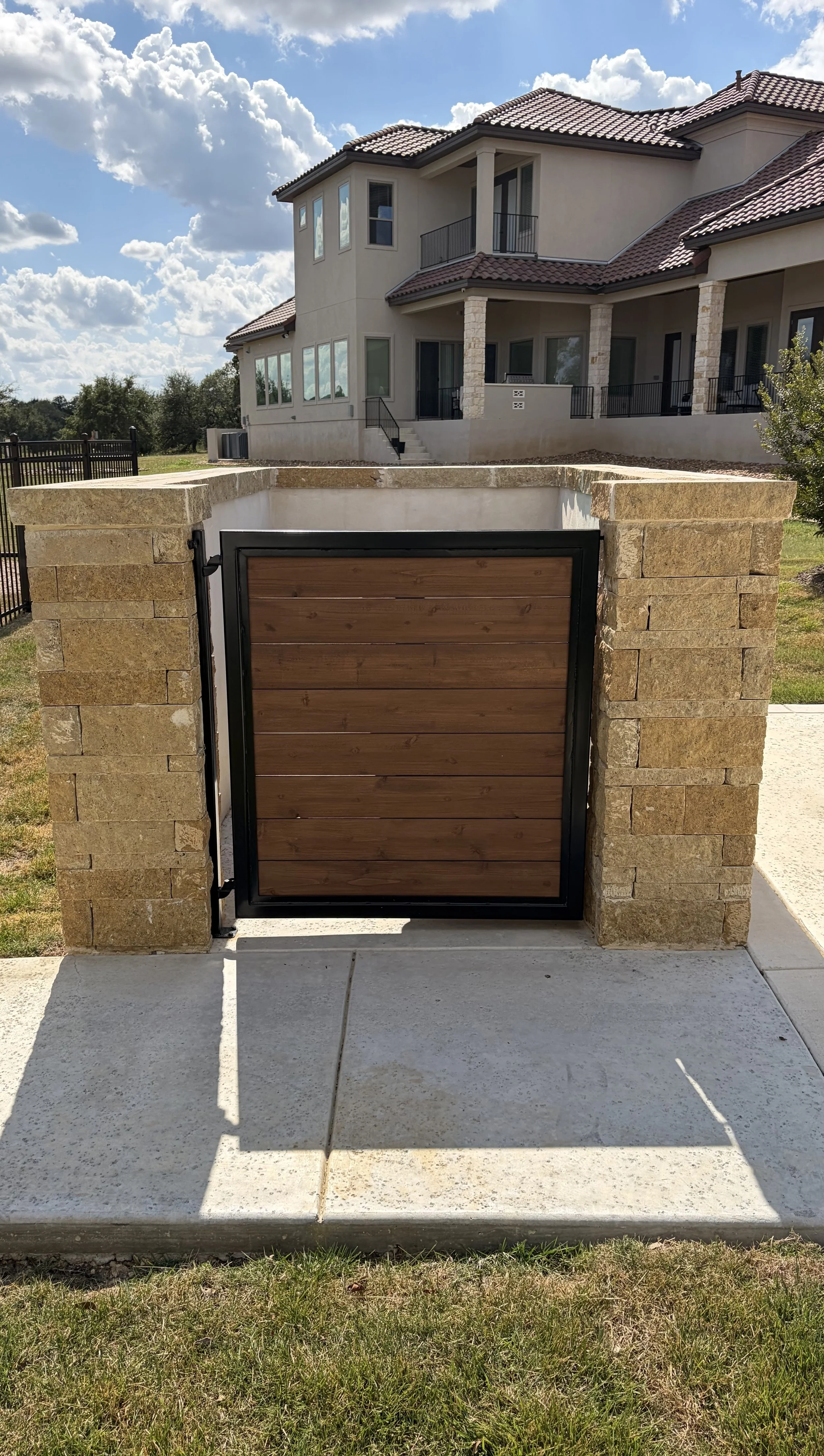 Steel framed gate with horizontals wood slats enclosing trash can bins.