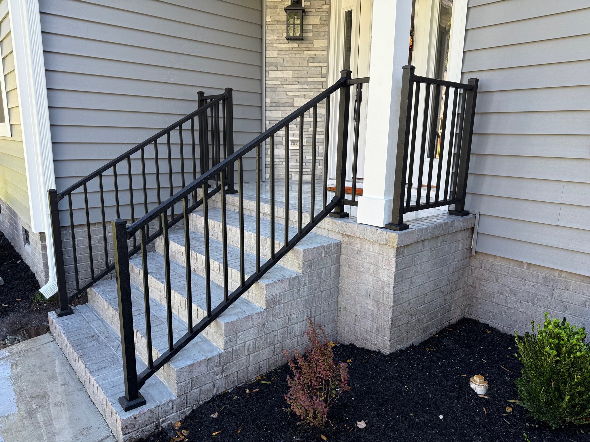 Front porch with stairs, black wrought iron railing a small porch area with steps and landing leading up to door of house.
