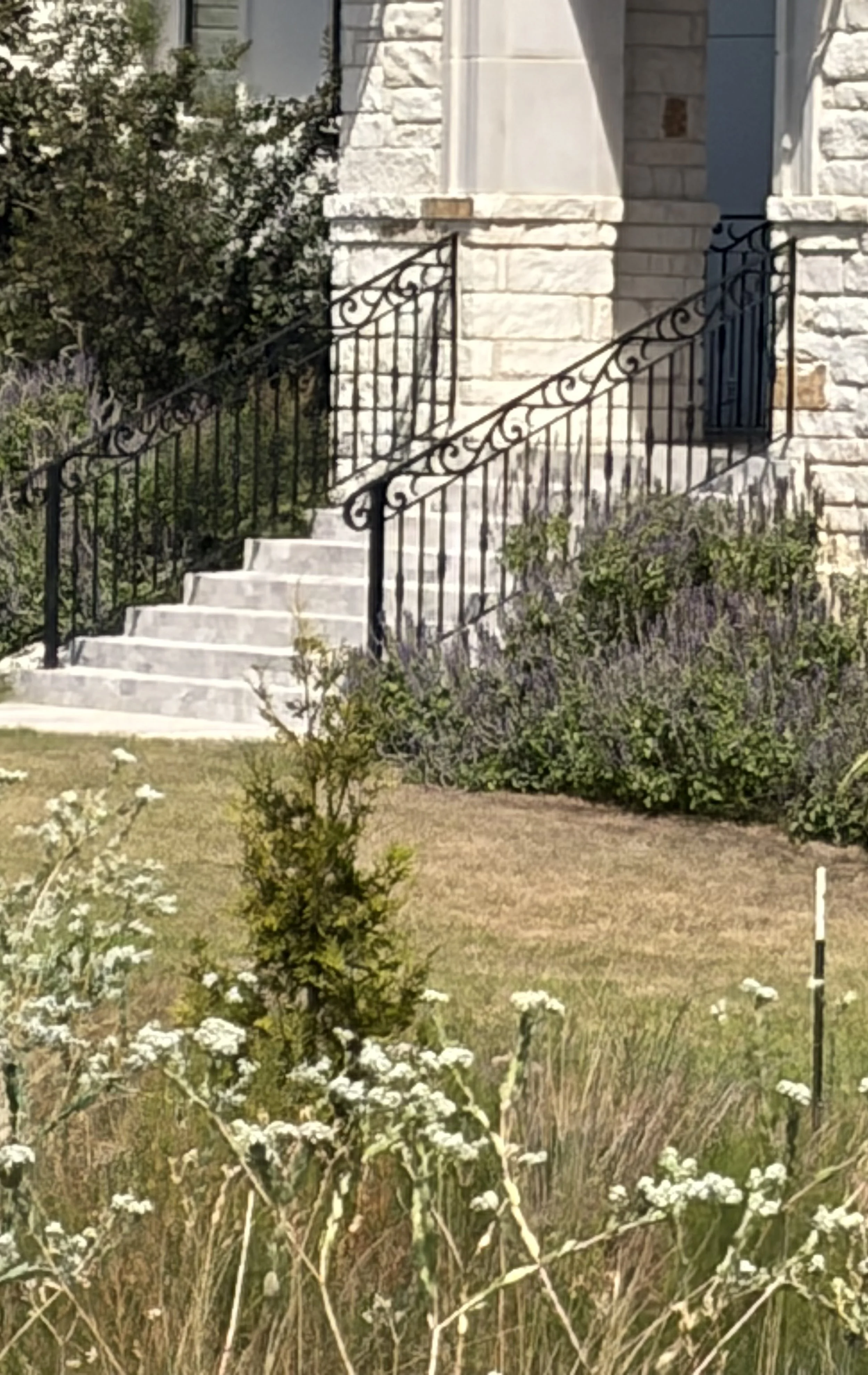 A stone house with a staircase and decorative black wrought-iron railings. 