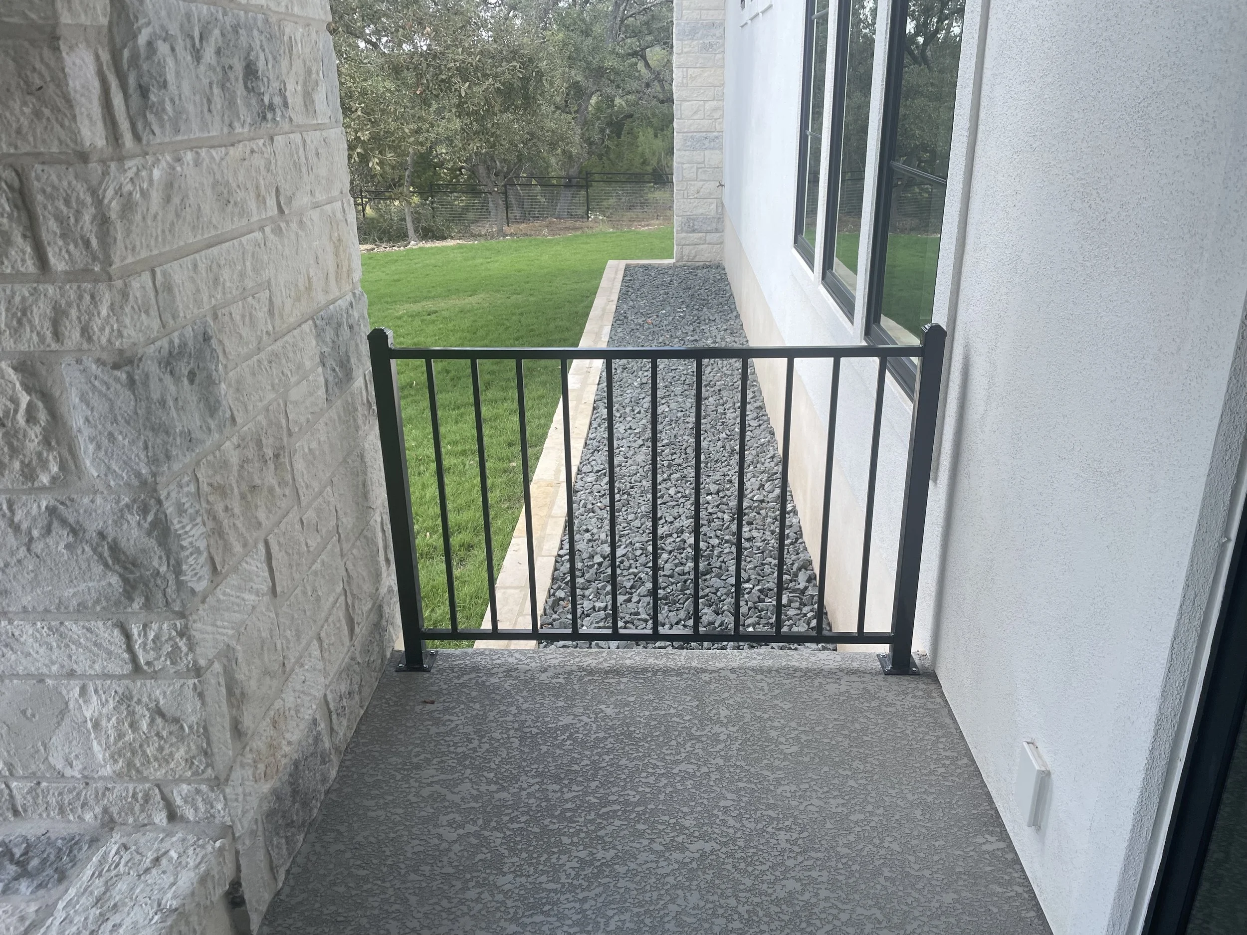Black wrought iron railing on between house and rock pillar on back porch.