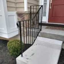Exterior of a house with concrete steps and a black ornamental wrought iron railing leading to the front door.