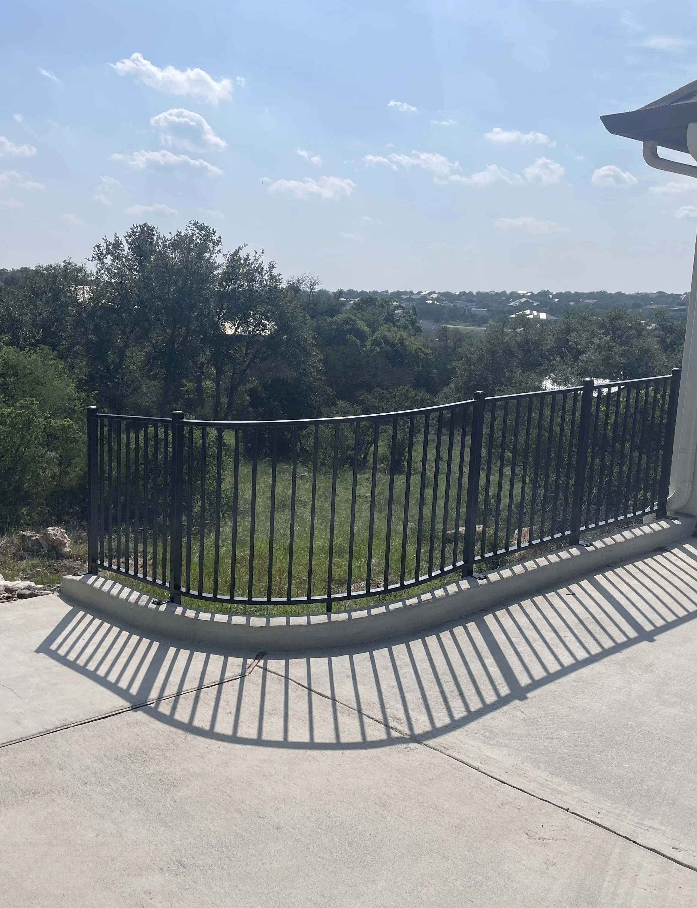 Black metal wrought iron railing on curved edge of driveway to garage of house.