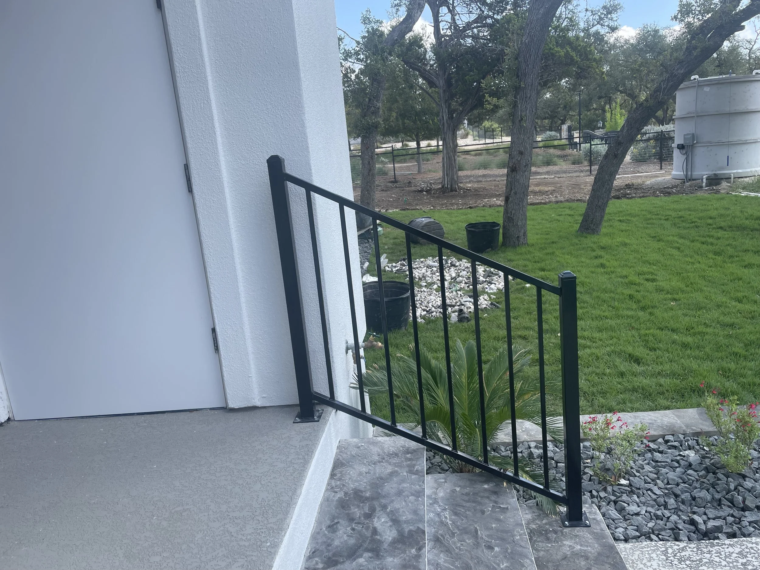 A white exterior wall with a black metal railing on a small porch on steps. 