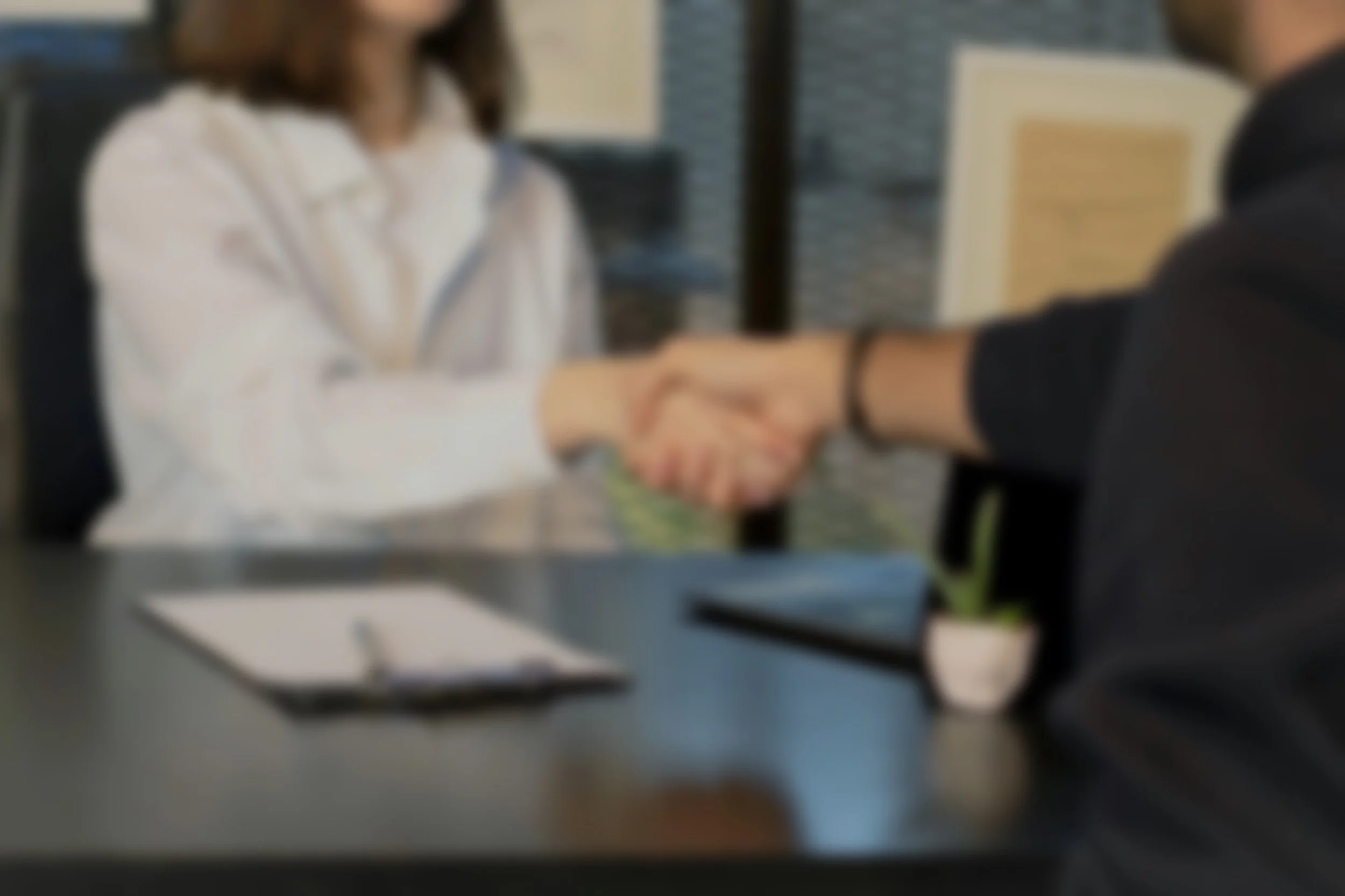 A blurred image of two people shaking hands in an office setting.