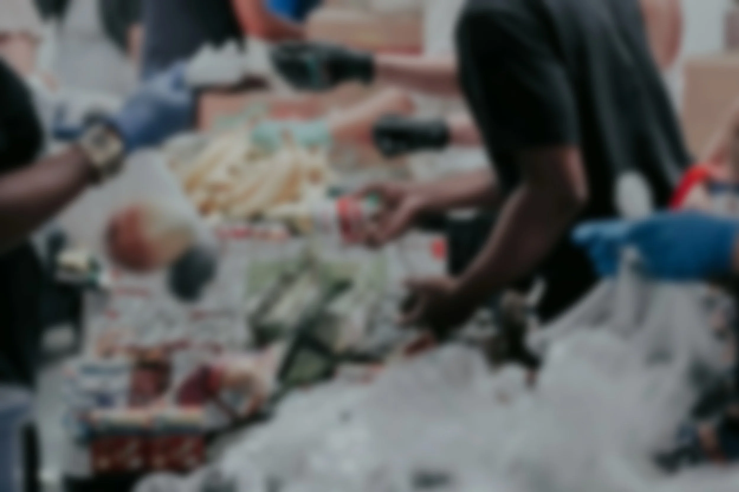 Blurred image of people shopping at a store, with shopping carts and items on the checkout conveyor belt.