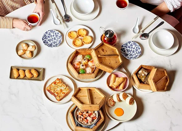 Table with dim sum dishes, bamboo steamers, teapot, cups, and desserts