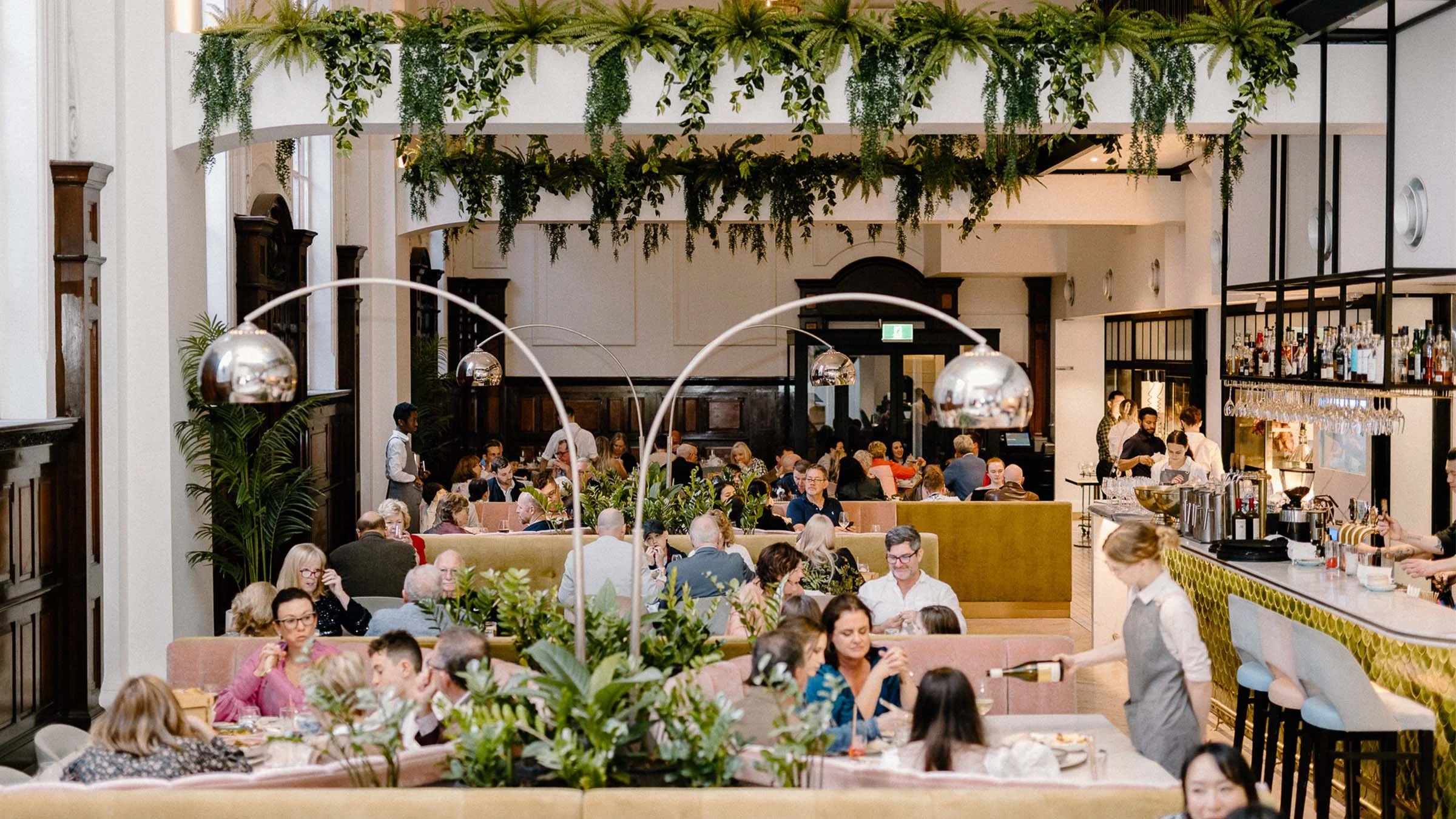 Donna Chang restaurant interior with people dining, bar area at the right with bartenders, overhead greenery, and modern decor.
