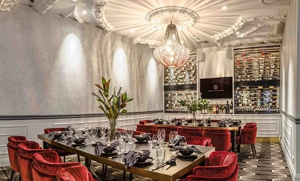 Elegantly decorated Donna Chang dining room in Brisbane CBD with a large wooden table, red velvet chairs, chandeliers, and a wine display wall.